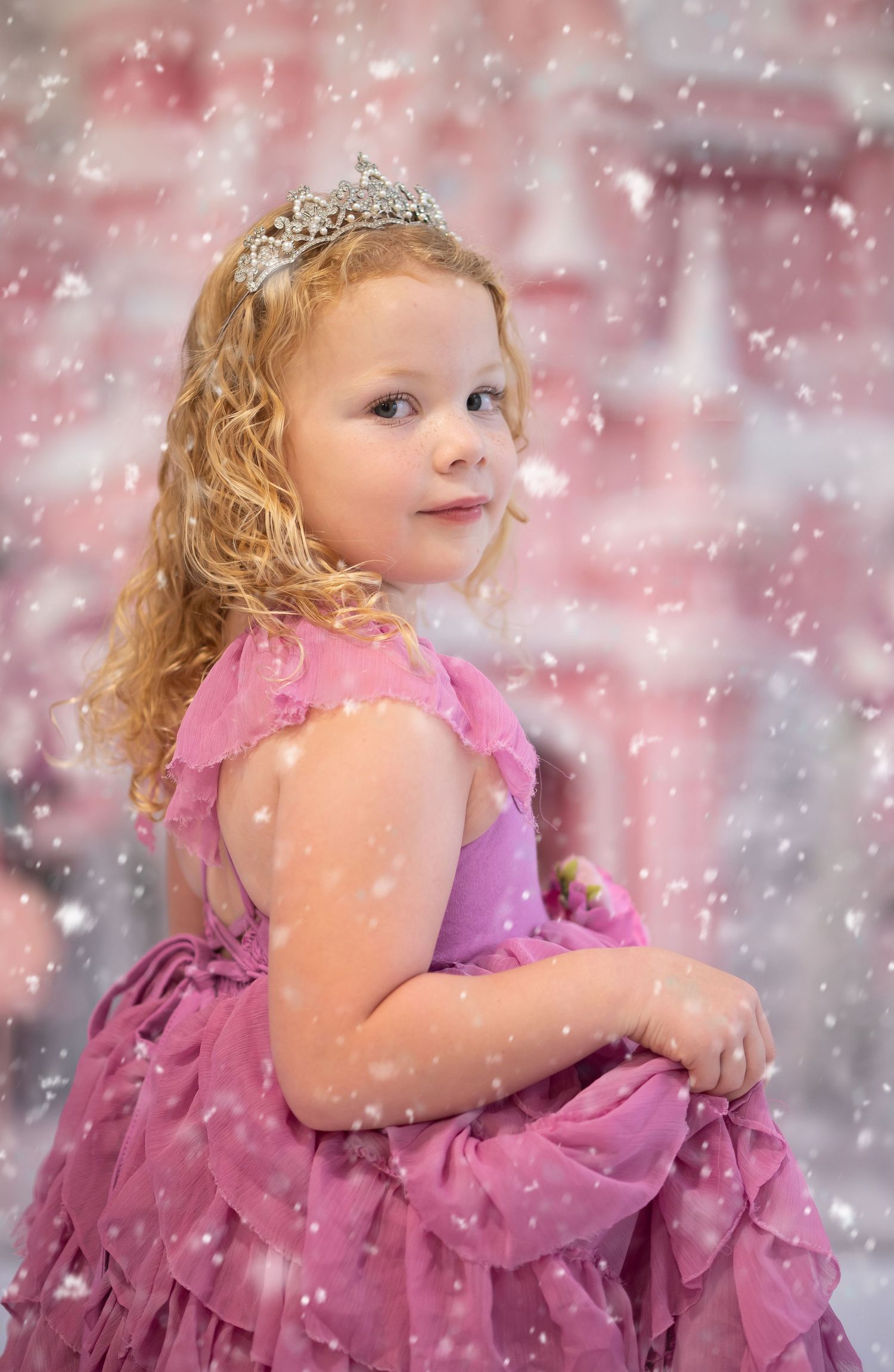 a little blonde girl in a frilly pink dress poses in front of a pink Christmas castle scene