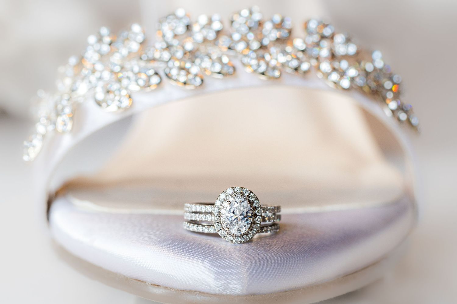 closeup of a bride's diamond wedding band set, poised on the edge of an elaborate white satin and gemstone studded wedding high heeled shoe.