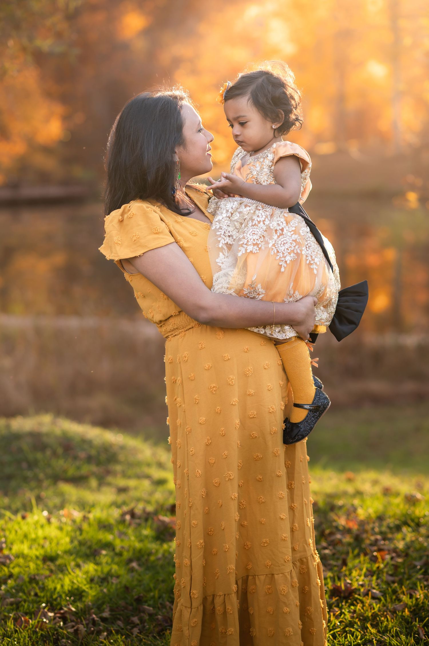 a mother and daughter in coordinated mustard yellow dresses pose for a portrait together in front of glorious fall scenery in Morgantown, WV