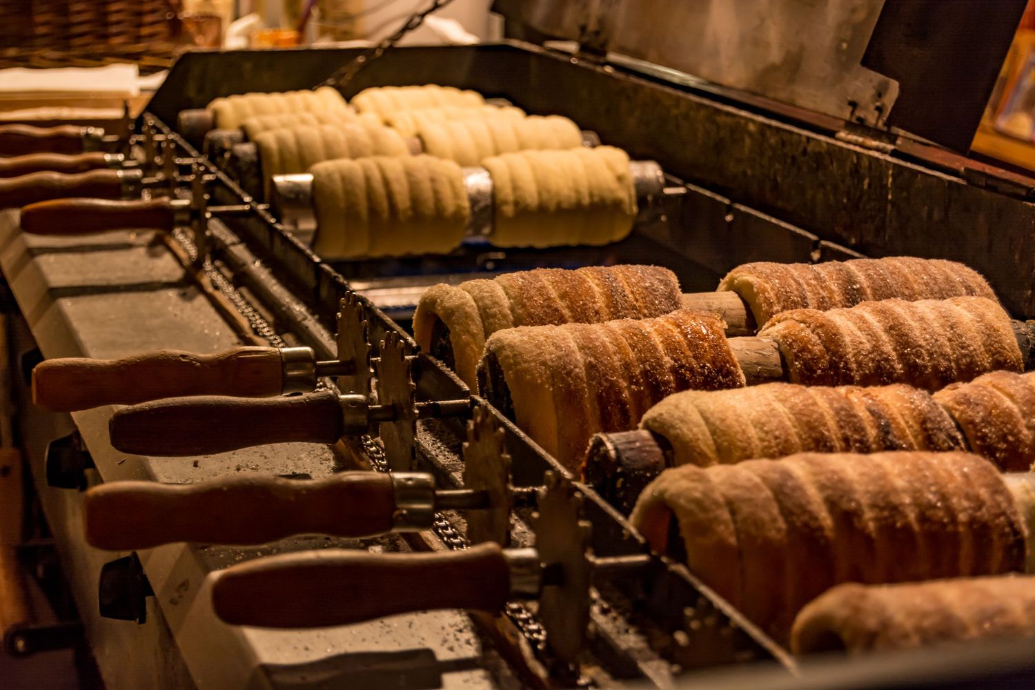 Trdelník pastries cooking on rotating spits over open flame at a traditional Czech street food market stall.