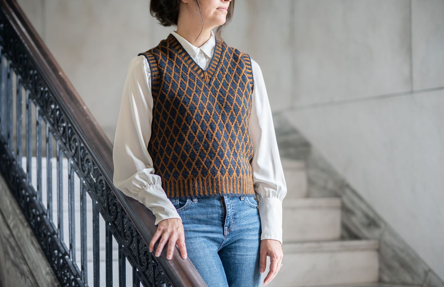 Product image of a female model wearing a patterned knit vest over a white blouse with jeans, standing on stone stairs by Rountree Stitchery