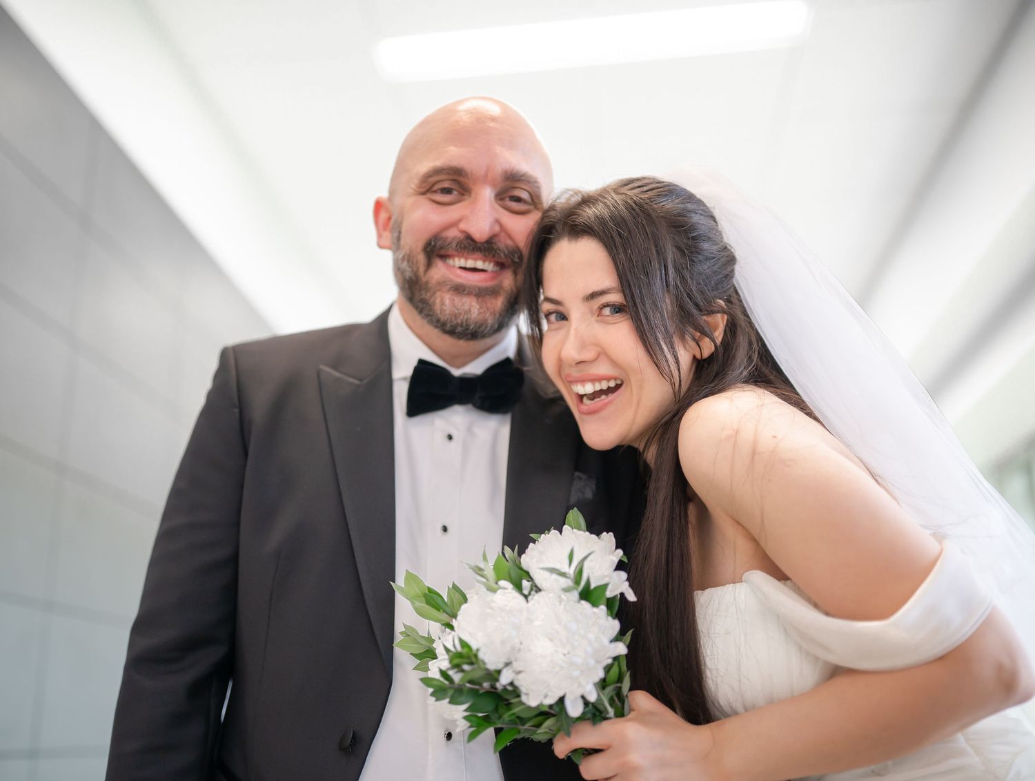 a bride and groom lean their heads together and laugh into the camera for a candid shot after a courthouse wedding in Morgantown, WV
