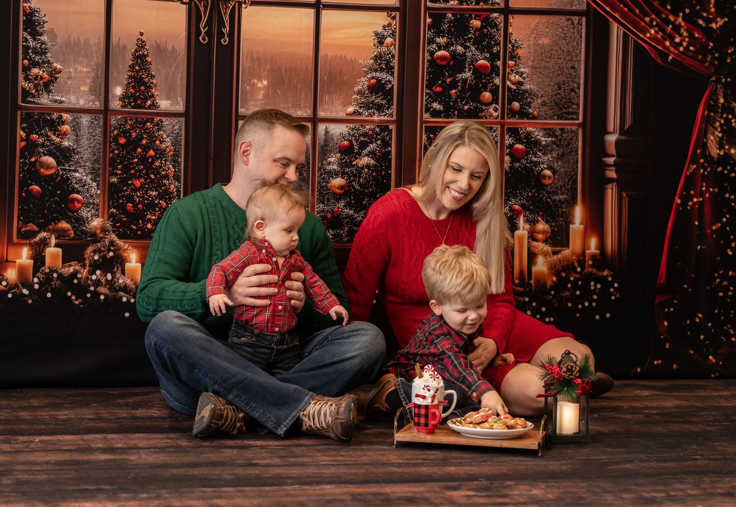 a young family of four sits in a cozy living room with hot cocoa and cookies, and a winter scene outside the window behind them