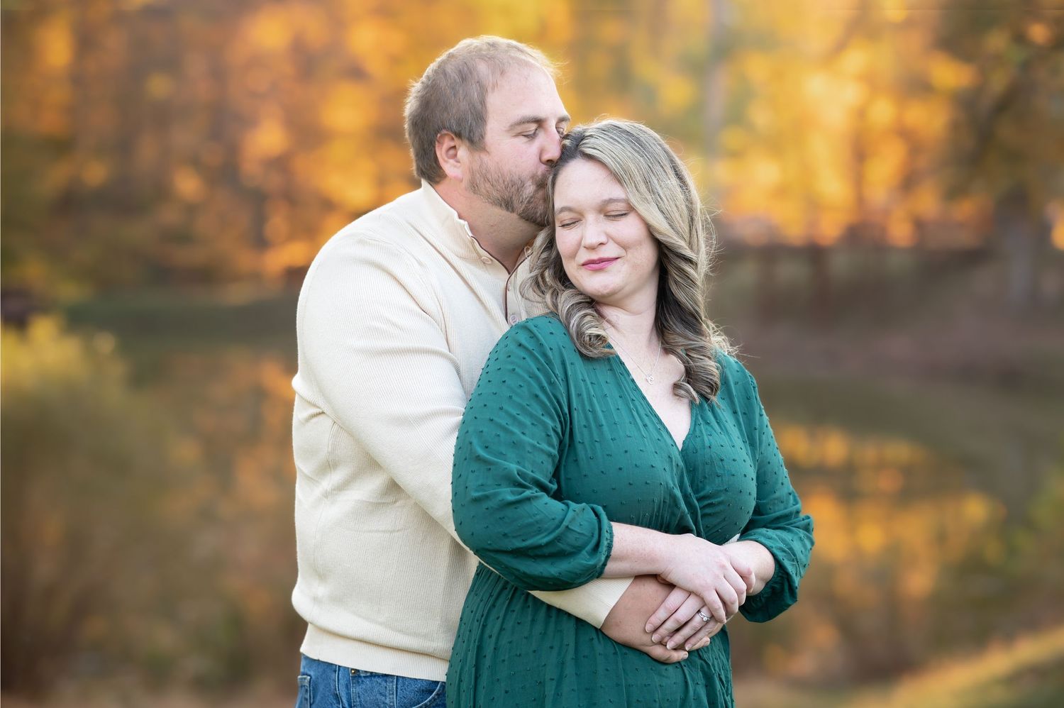 a husband and wife embrace and pose for a portrait as he kisses the side of her head, and she smiles