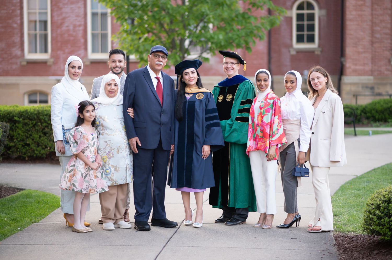 a college graduate poses with her extended family, friends, and professor for a portrait on WVU campus