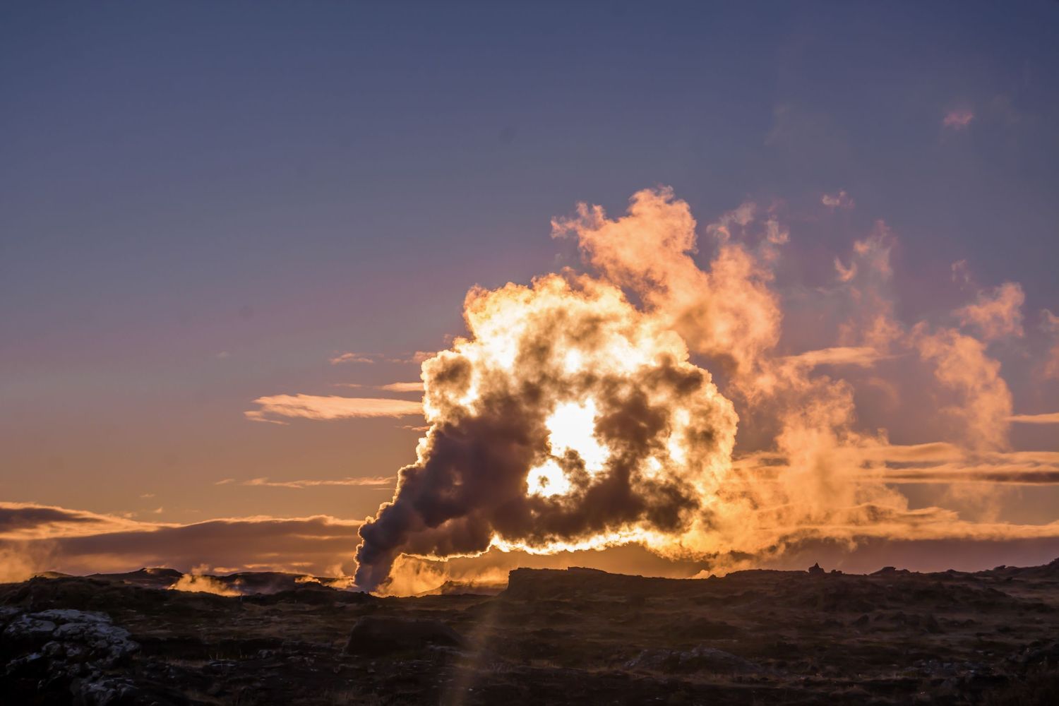 Dramatic geothermal steam plume backlit by golden sunset light against a deep blue sky in Iceland.