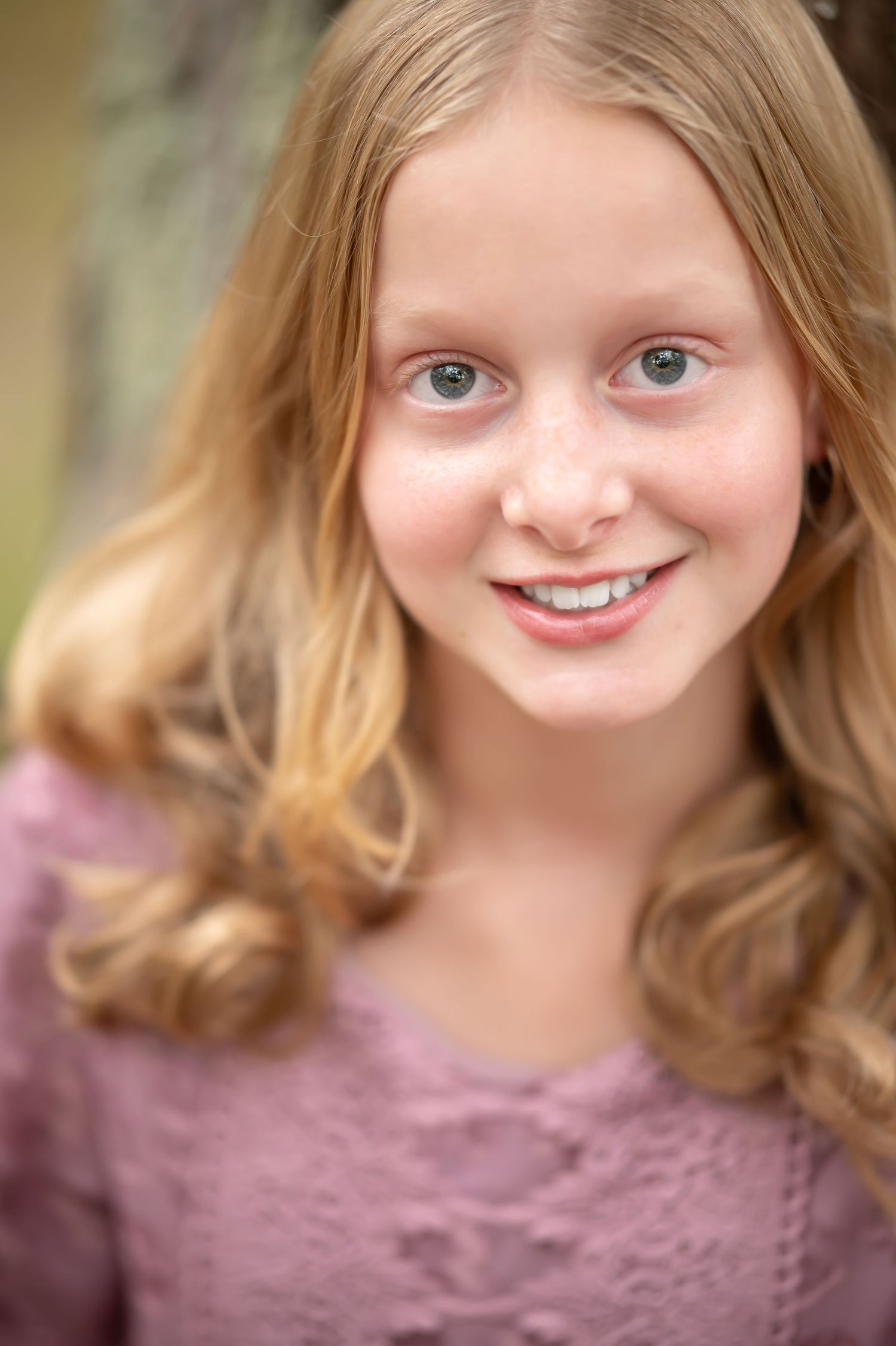 closeup portrait of a young girl with golden blonde hair and blue eyes in a pink dress, smiling at the camera