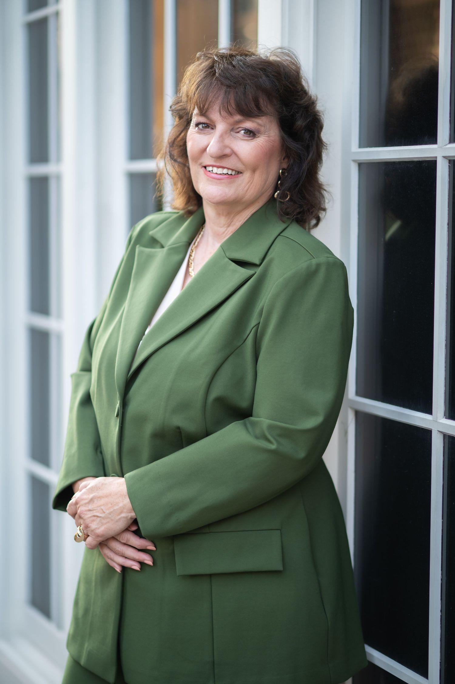 branding image of a female financial coach in a green business suit leaning against a white window