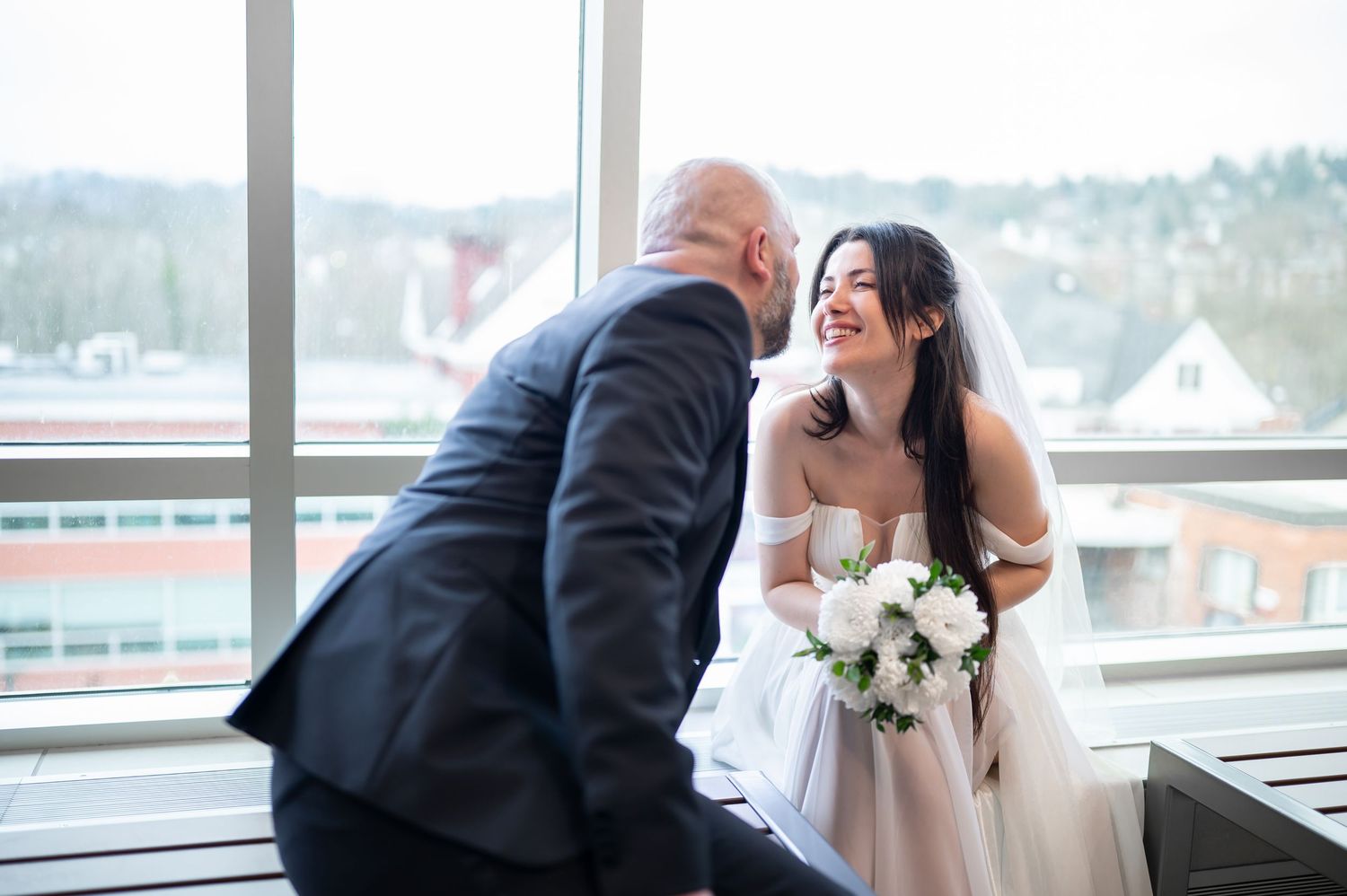 a bride and groom sit and tease and laugh together after their courthouse wedding with downtown Morgantown WV visible in the background