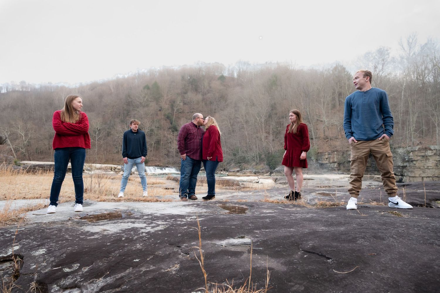 a family of five wearing blue and red strikes a vogue pose on large rocks in front of a waterfall in Valley Falls State Park, WV