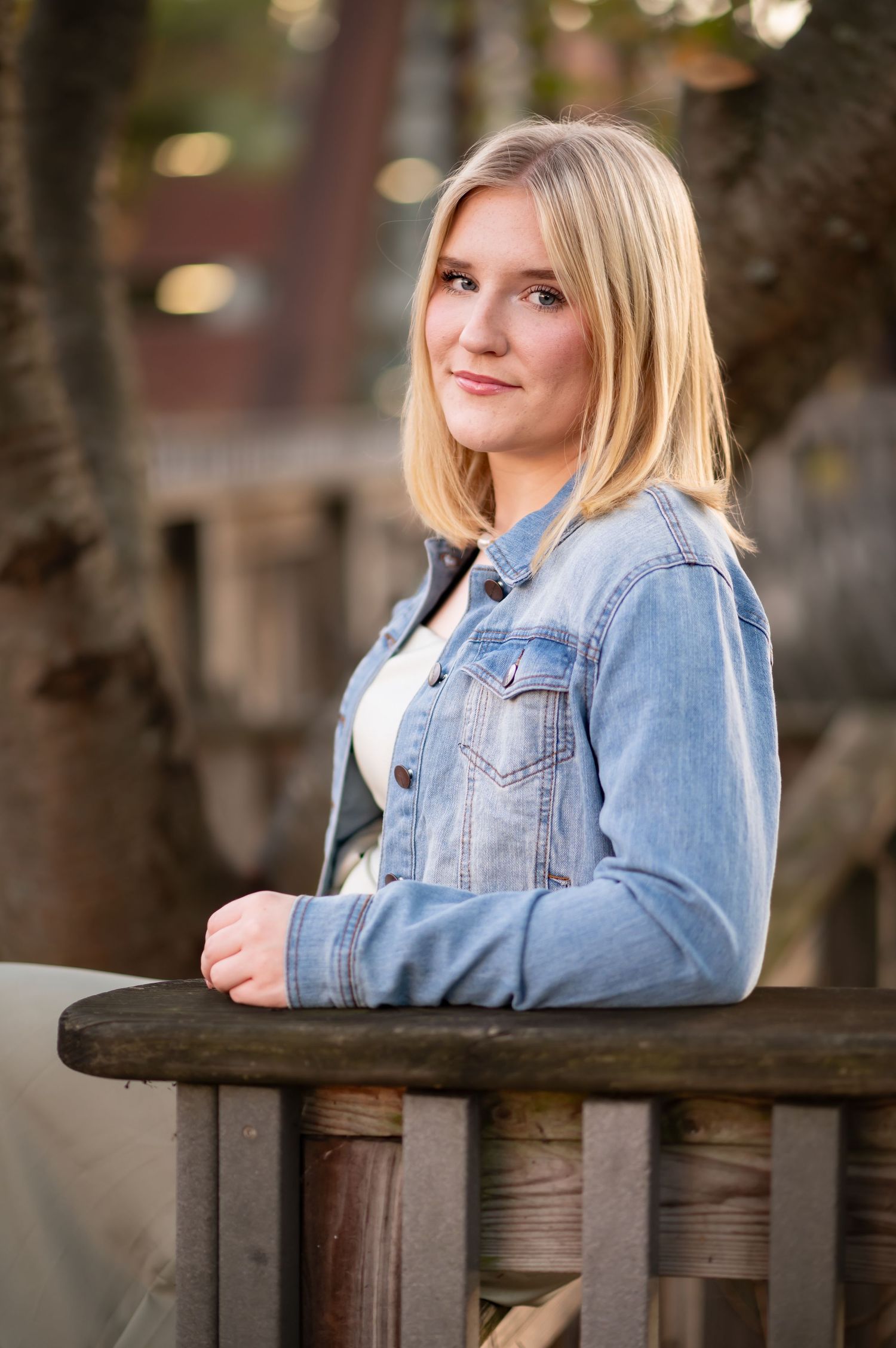 a young blonde woman in a denim jacket leans her elbow against a railing and smiles at the camera in downtown Morgantown, WV
