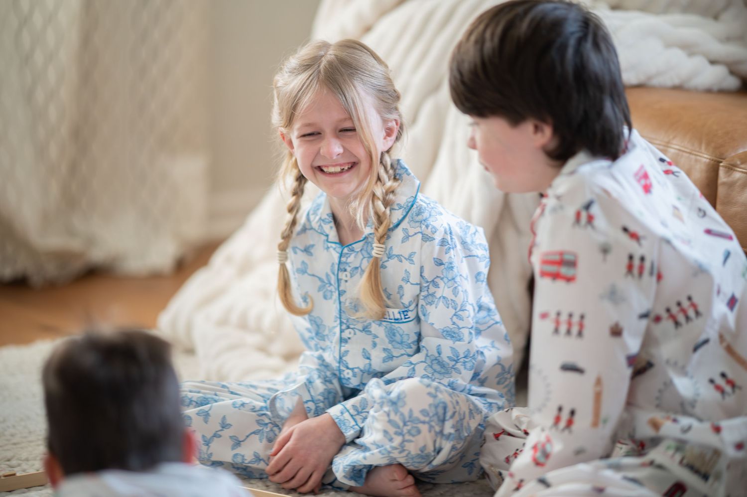 a little girl and boy in colorful pajamas sit on a white rug playing a game and laughing together during a lifestyle commercial photoshoot
