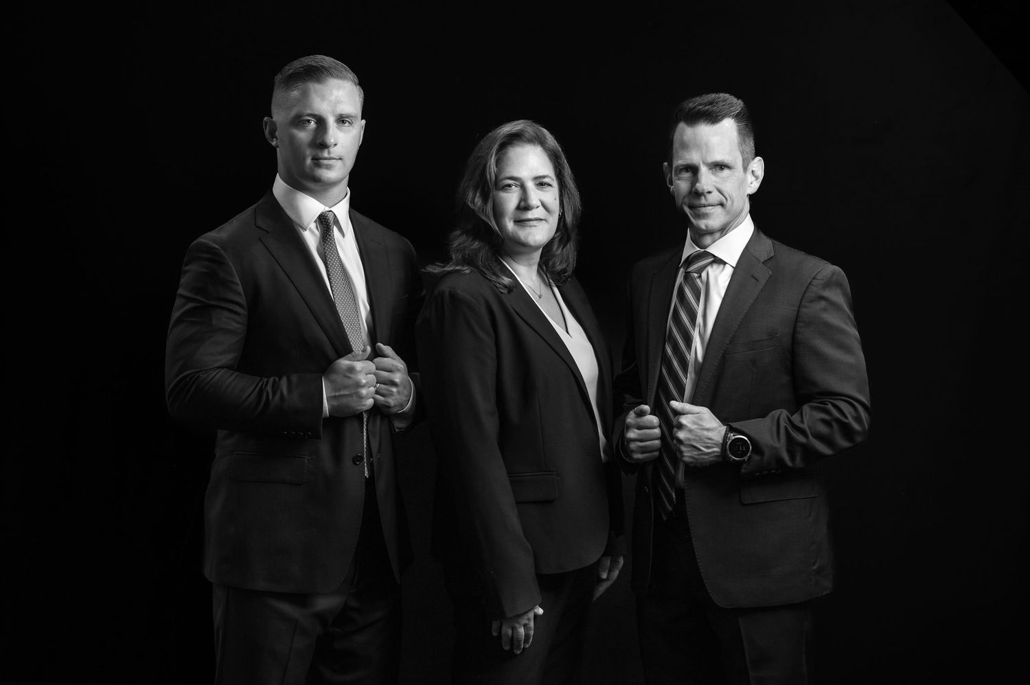 dramatic black and white group shot of three lawyers posing together in business suits against a rich black background; Morgantown, WV