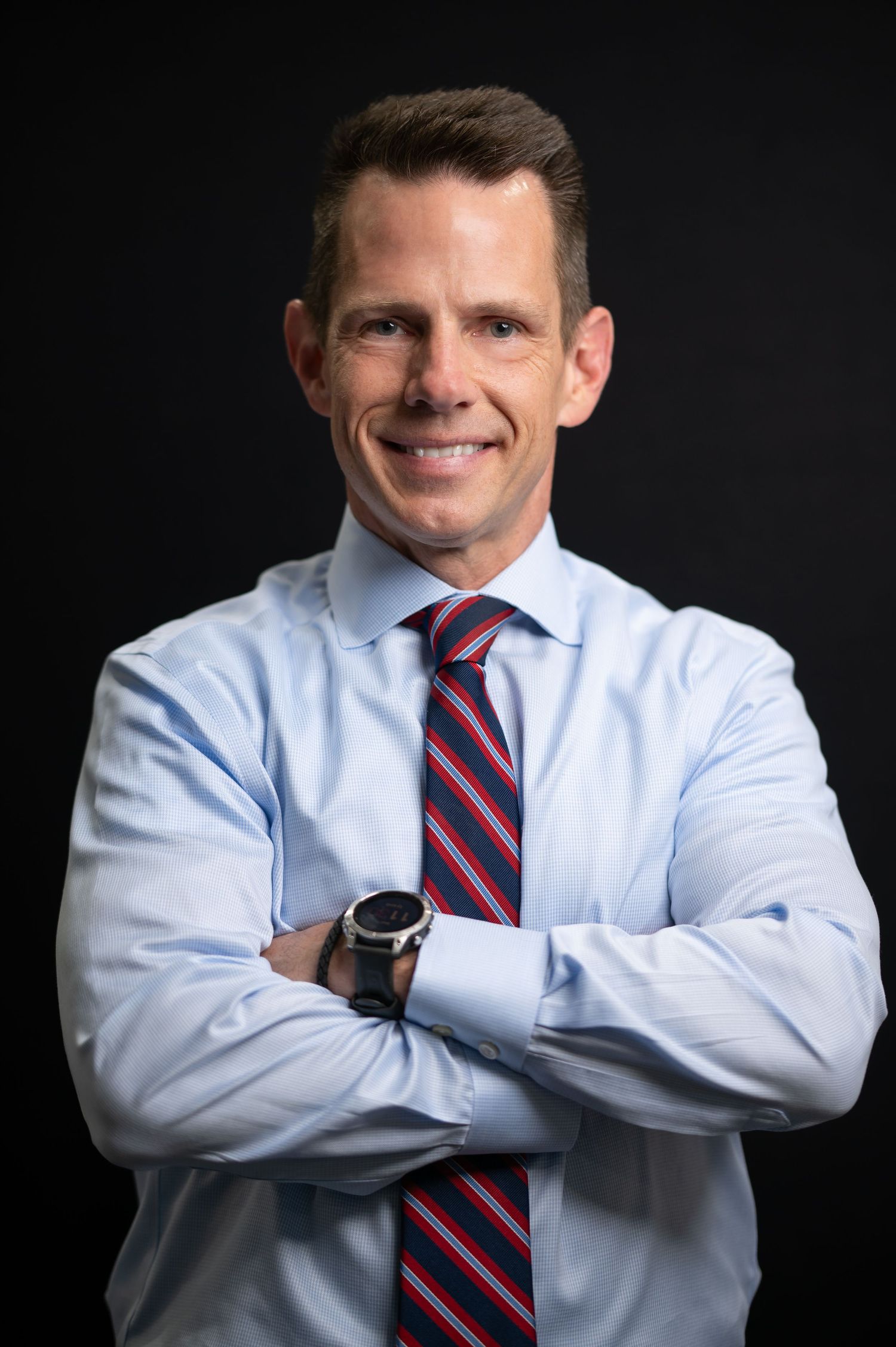 dramatic headshot of a male lawyer in a blue dress shirt, posing with crossed arms and a confident smile, against a black background