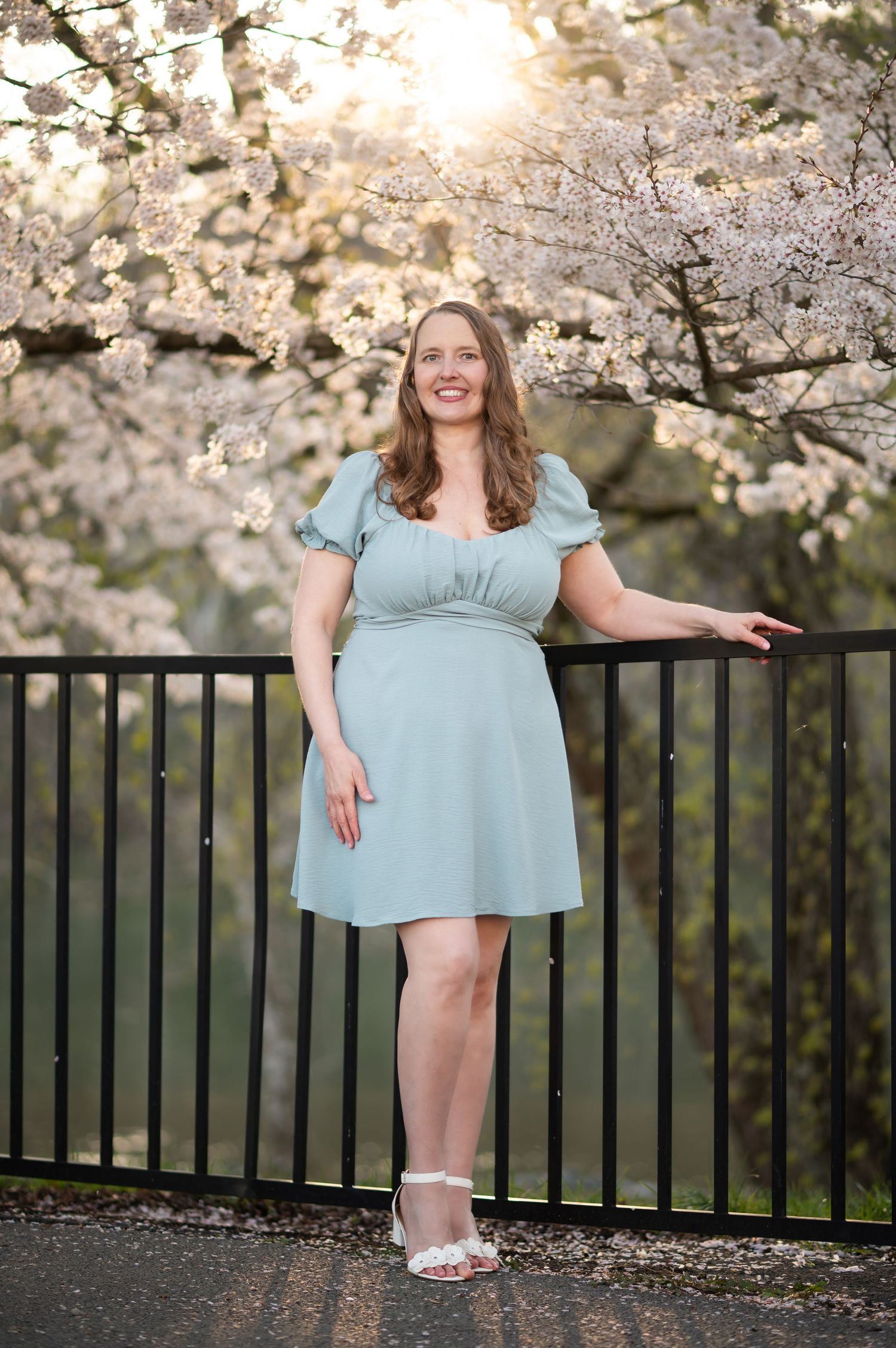 a pretty woman in a light blue dress poses for a portrait in front of flowering pink cherry trees in downtown Morgantown, WV