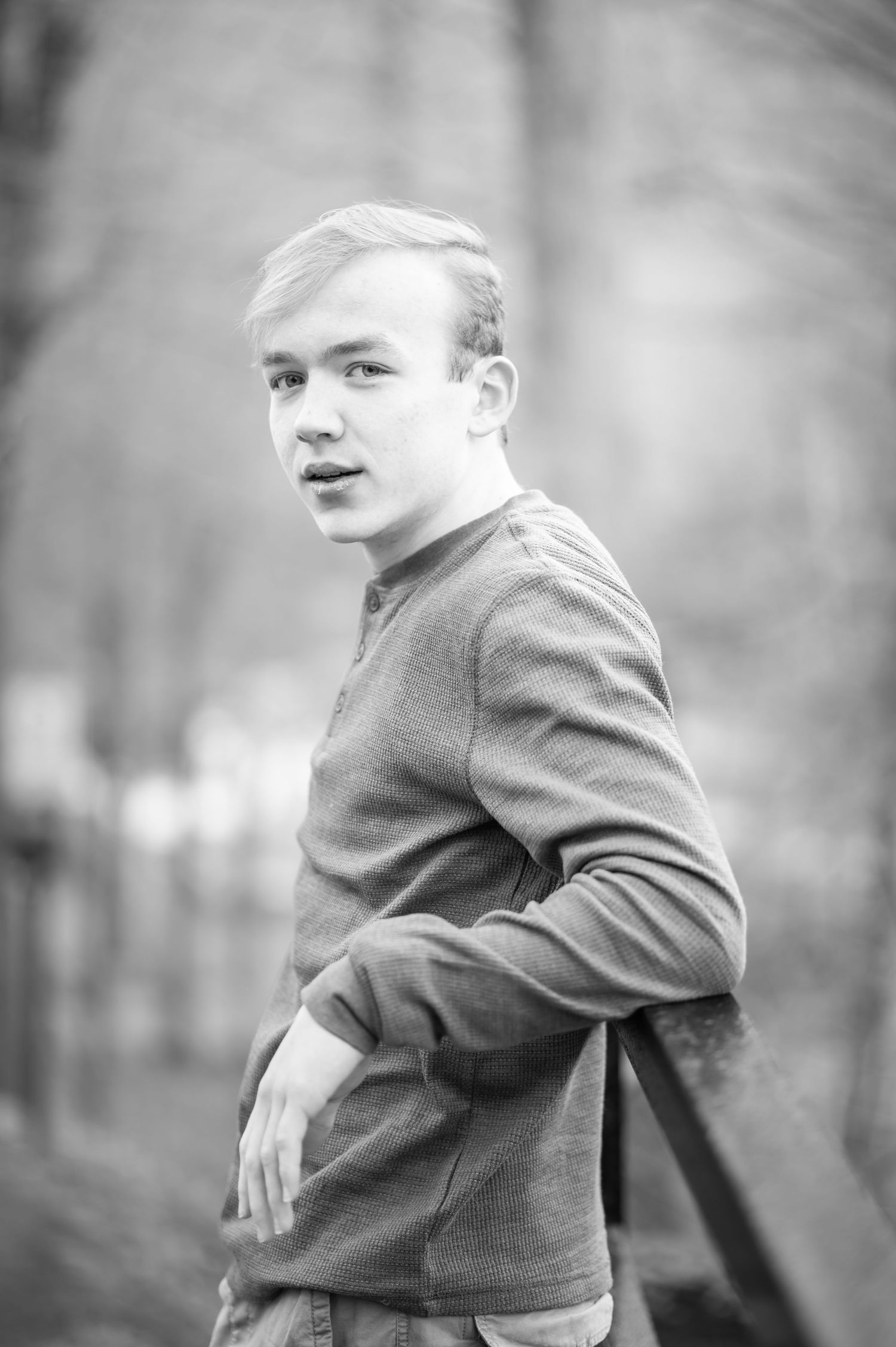 black and white portrait of a young man leaning against the railing of a wooden walkway with forest in the background