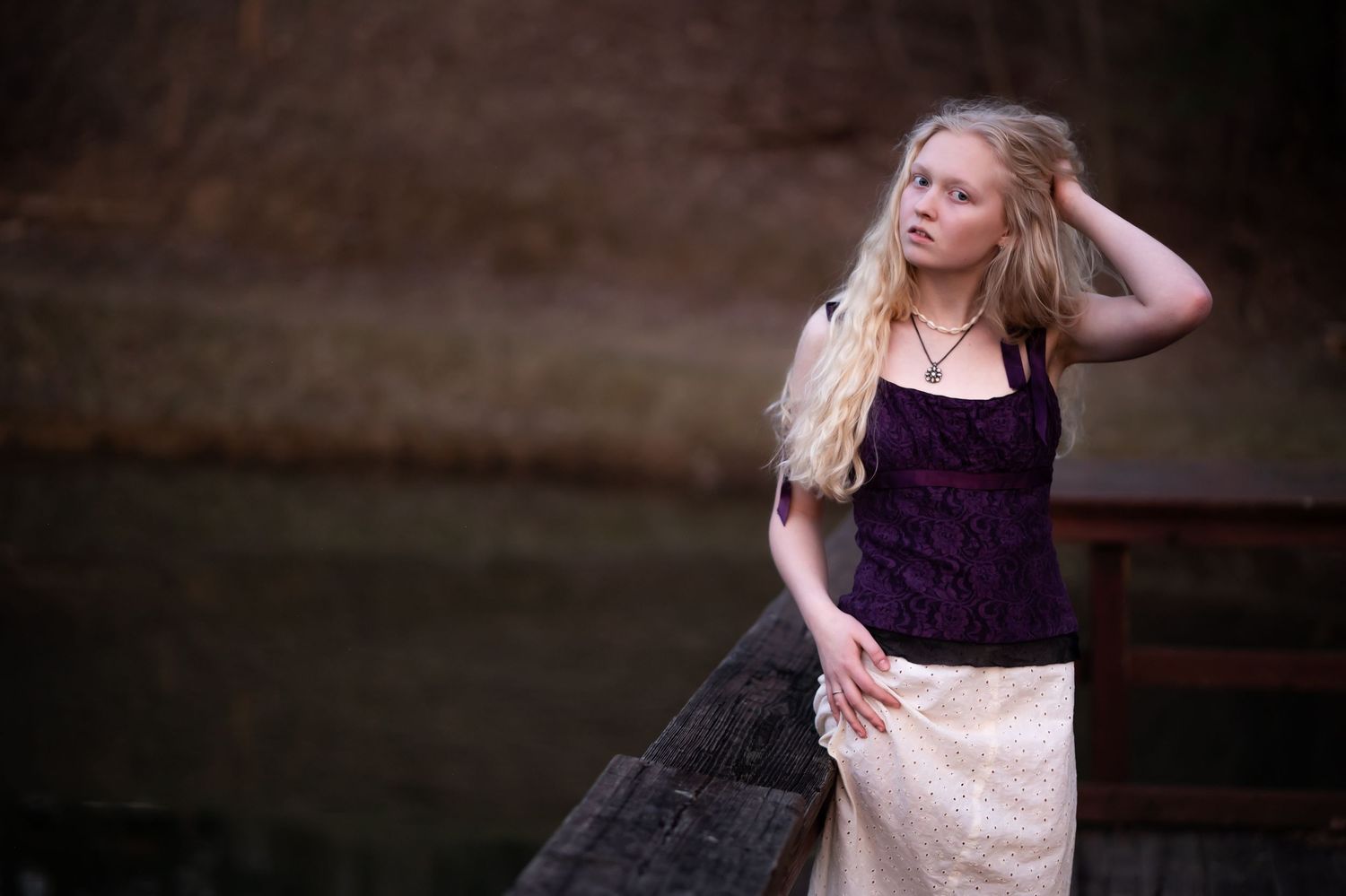 vogue-style senior portrait of a pretty blonde senior student in a purple top and white skirt, with a lake in the background.