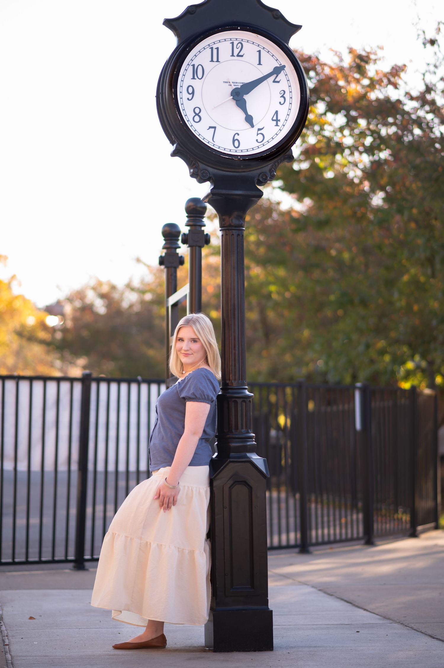 a blonde young woman leans against a tall black clock in downtown Morgantown, WV, and smiles for a picture