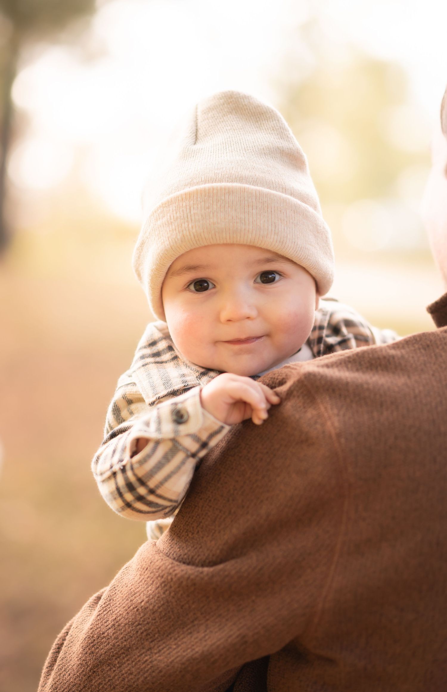 a little boy in a plaid shirt and fall toboggan peeks over his fathers shoulder and smiles during a mini session in Morgantown, WV