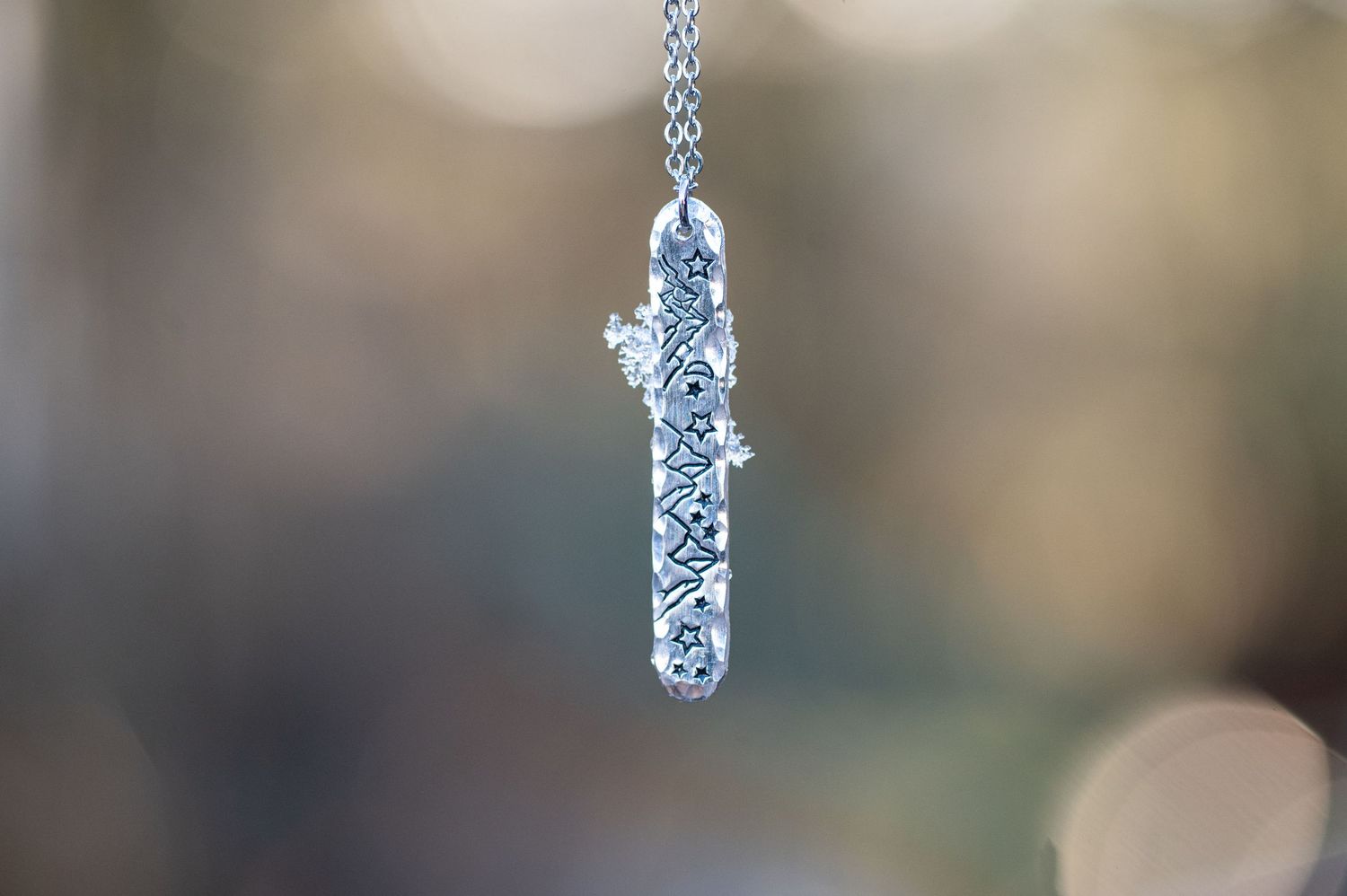 product image of a hammered silver hand-stamped pendant necklace with ice crystals clinging to it, hanging in front of a soft background