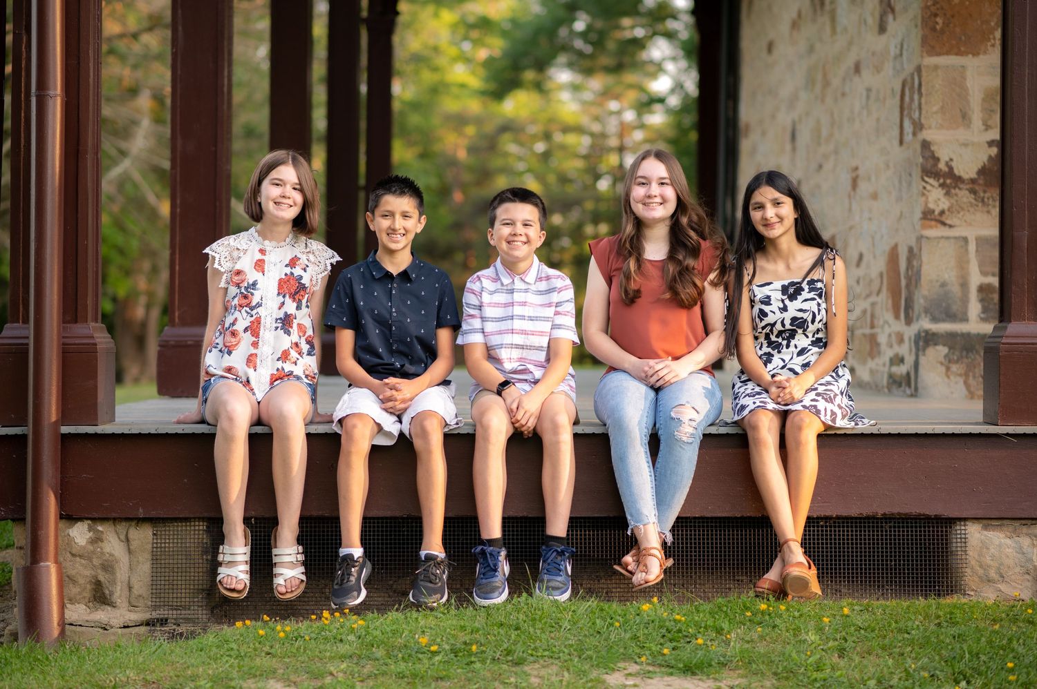 Five smiling teenage siblings pose seated for a portrait on the edge of the porch at Albert Gallatin house in Friendship Hill in PA.