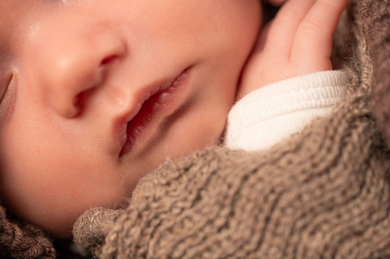 Close-up of a peaceful sleeping newborn baby wrapped in a soft brown knit blanket.
