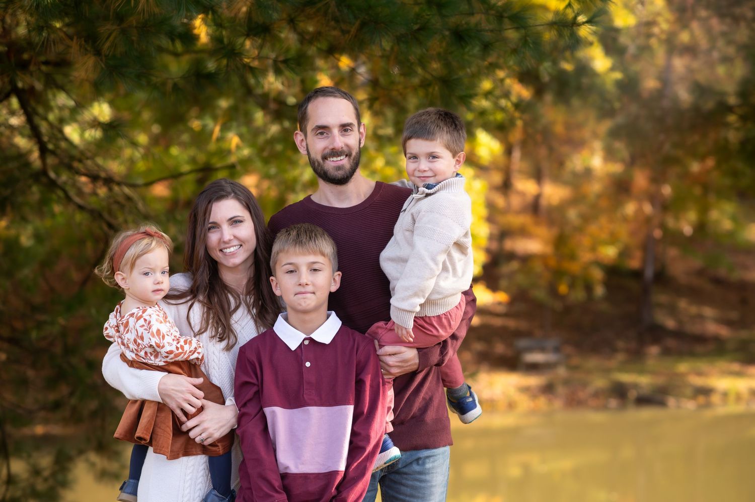 a family of five dressed in coordinating outfits in purples and ivory stand together for a fall portrait