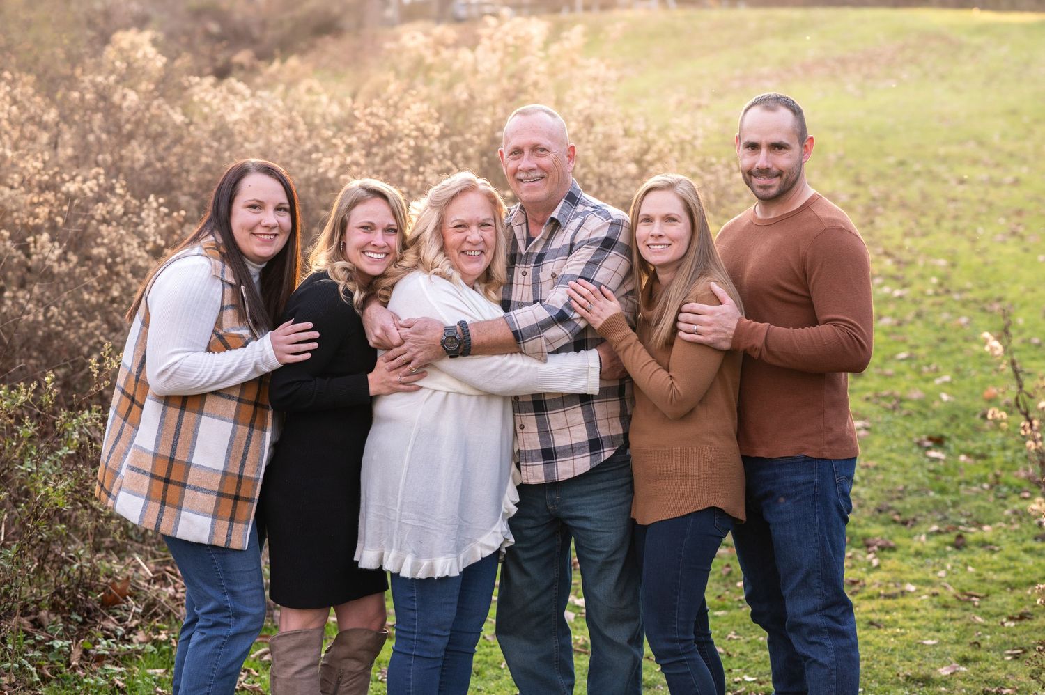 parents pose with their four adult children in a clearing with tall golden grass in the background
