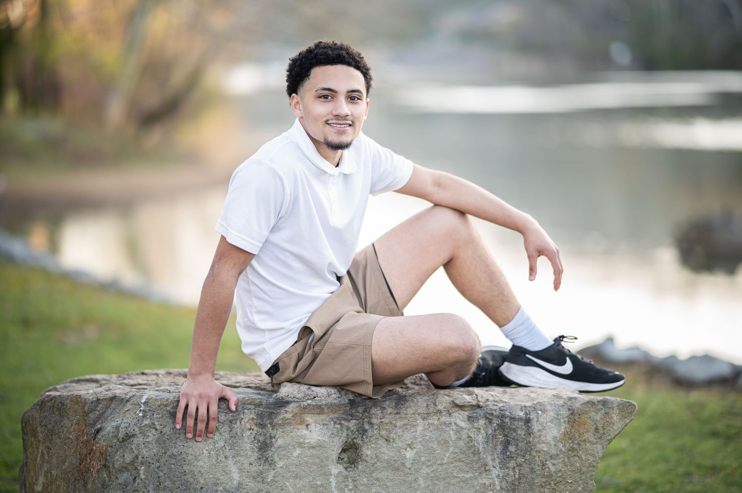 a young graduate student in a white shirt and khakis poses for a portrait on a large rock with the Monongalia River in the background