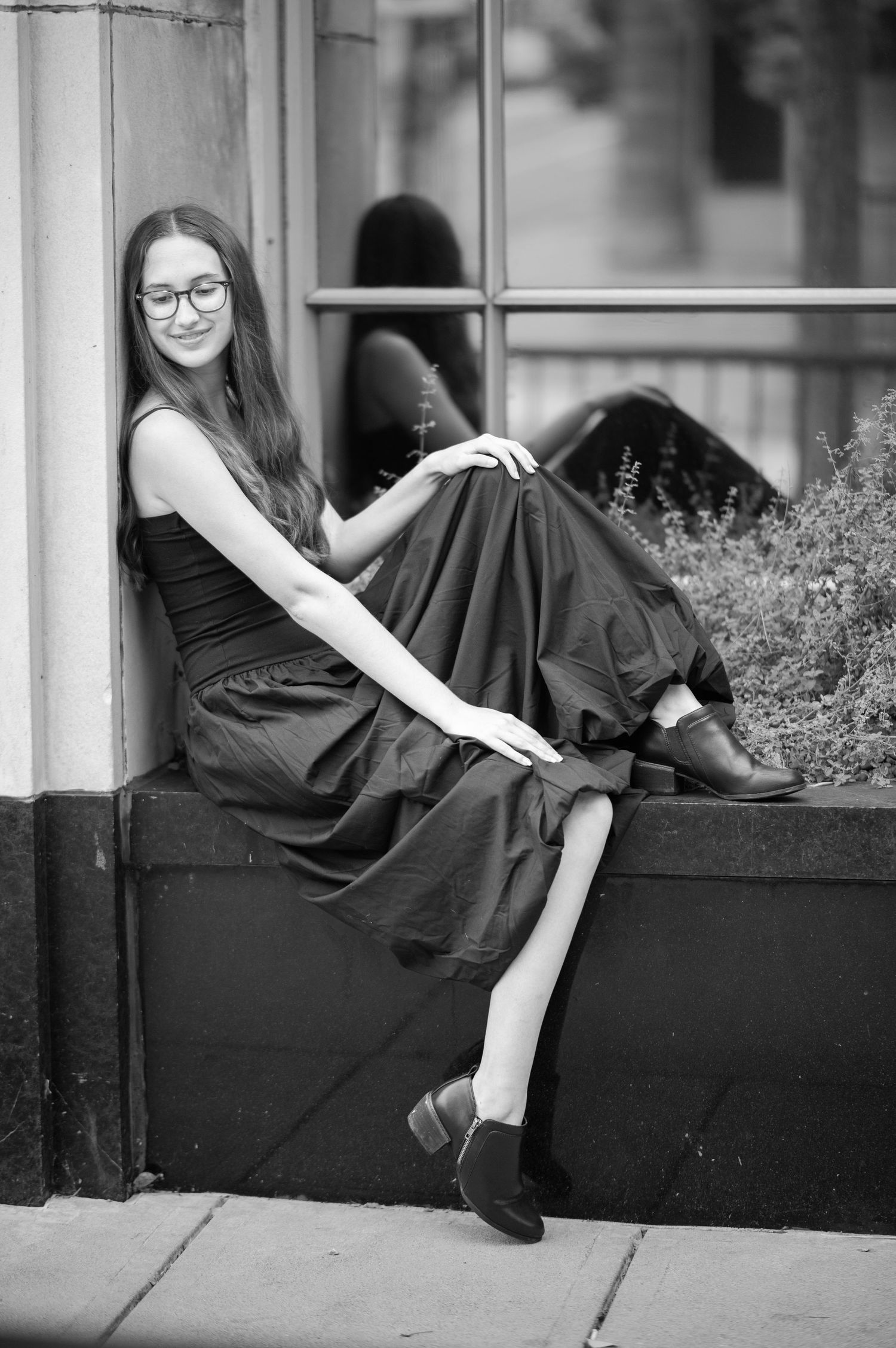 a senior student in a long black dress poses casually in the window of a downtown shop on High Street in Morgantown, Wv