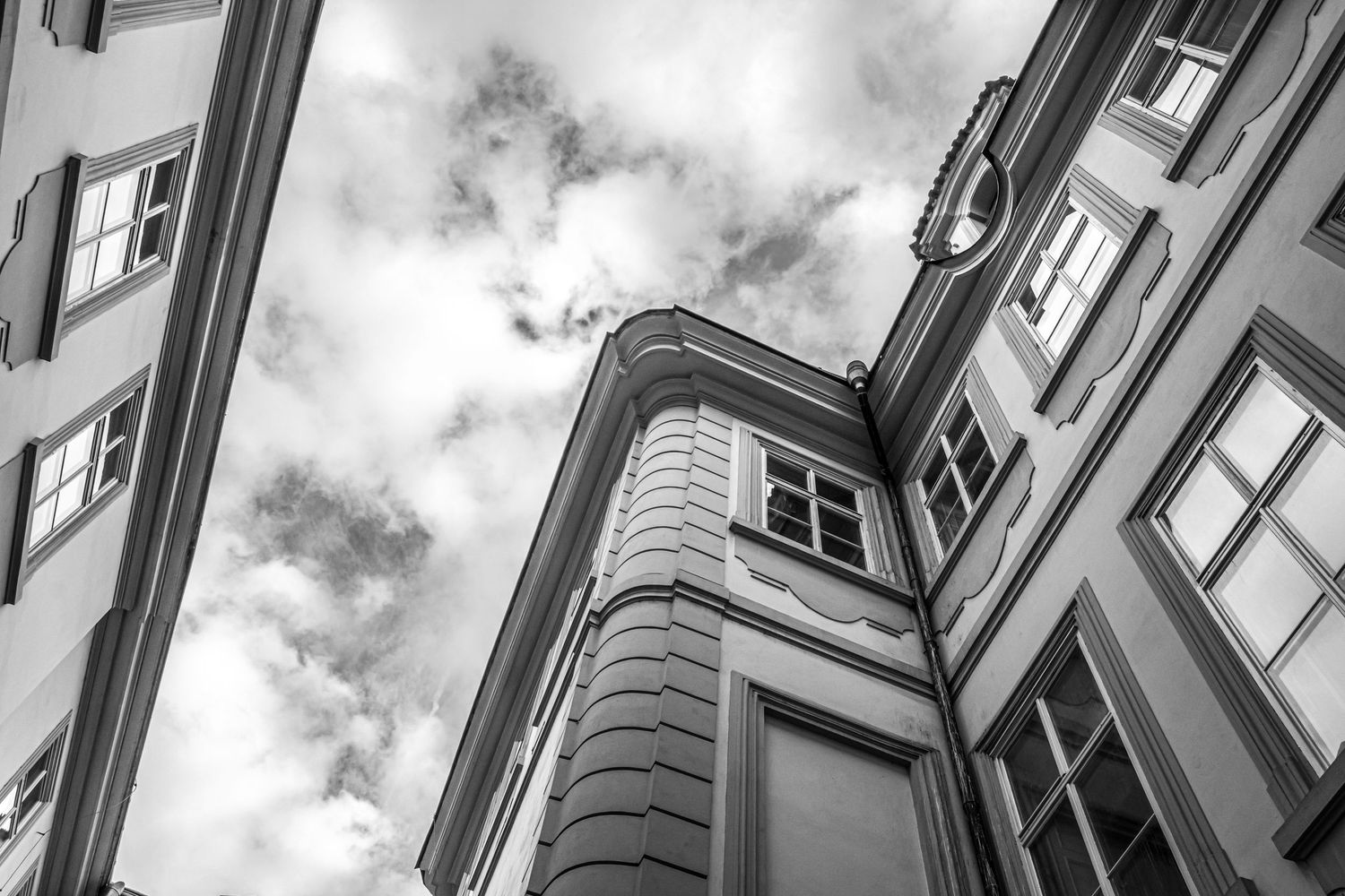 Black and white low-angle view of classic European building corner with ornate architecture against cloudy sky.