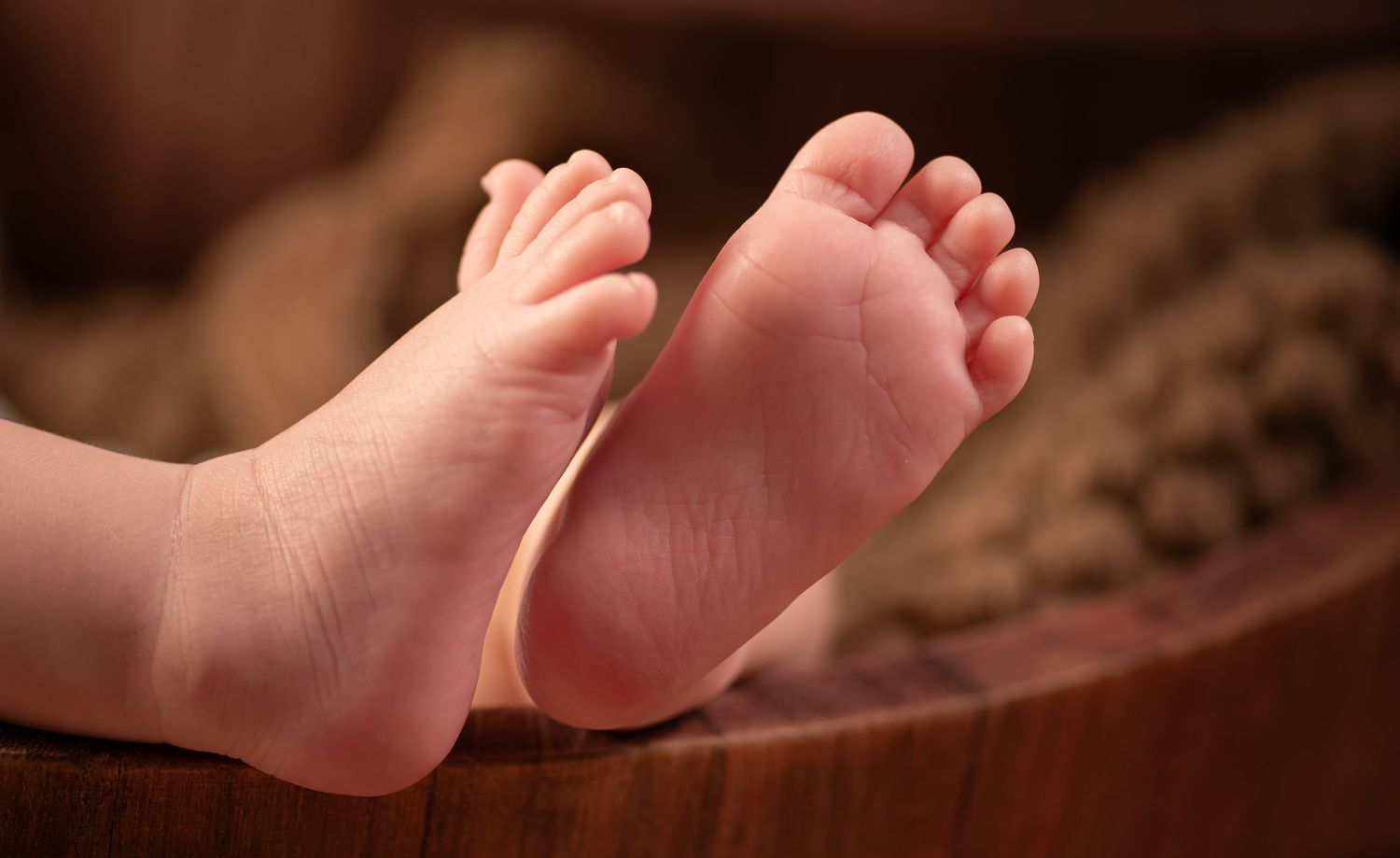 Close-up of soft, tiny newborn baby feet resting on a wooden surface with warm bokeh background.