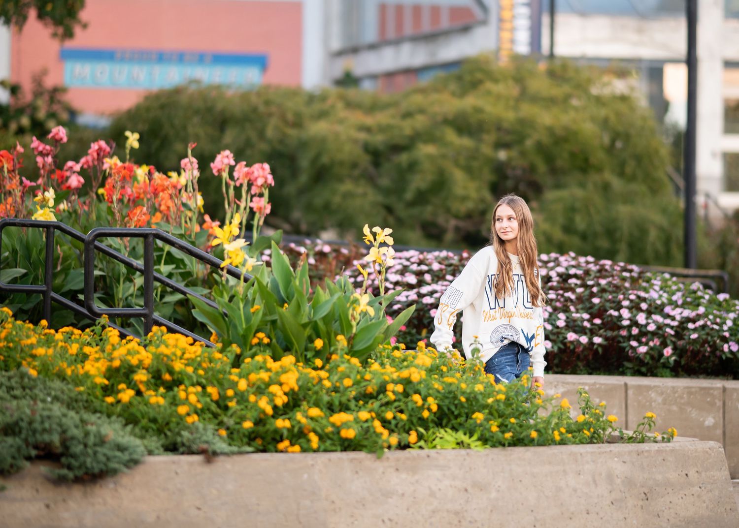 high school senior poses for a portrait amid brilliant blooming flowers on WVU campus in front of the Mountain Lair during a senior session