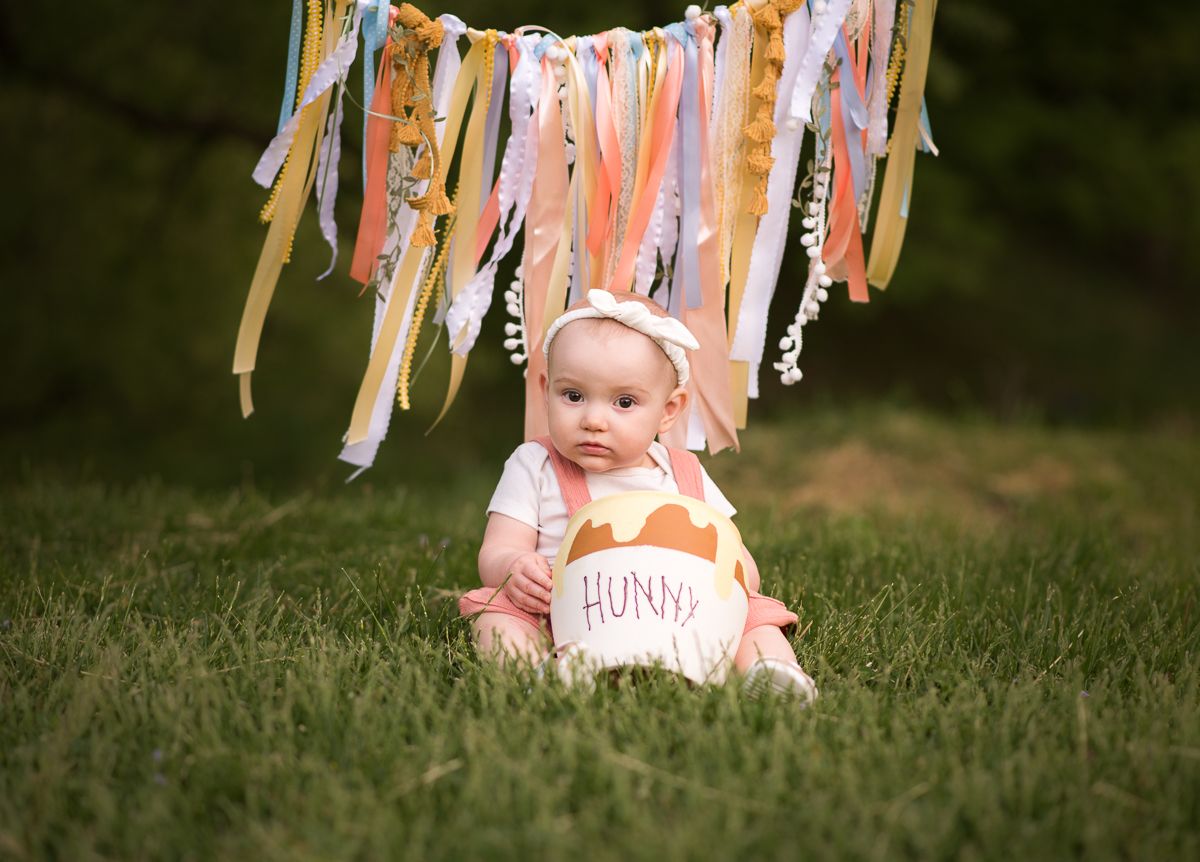 a little girl sits in the grass with a smash cake and a streamer banner hanging in the background