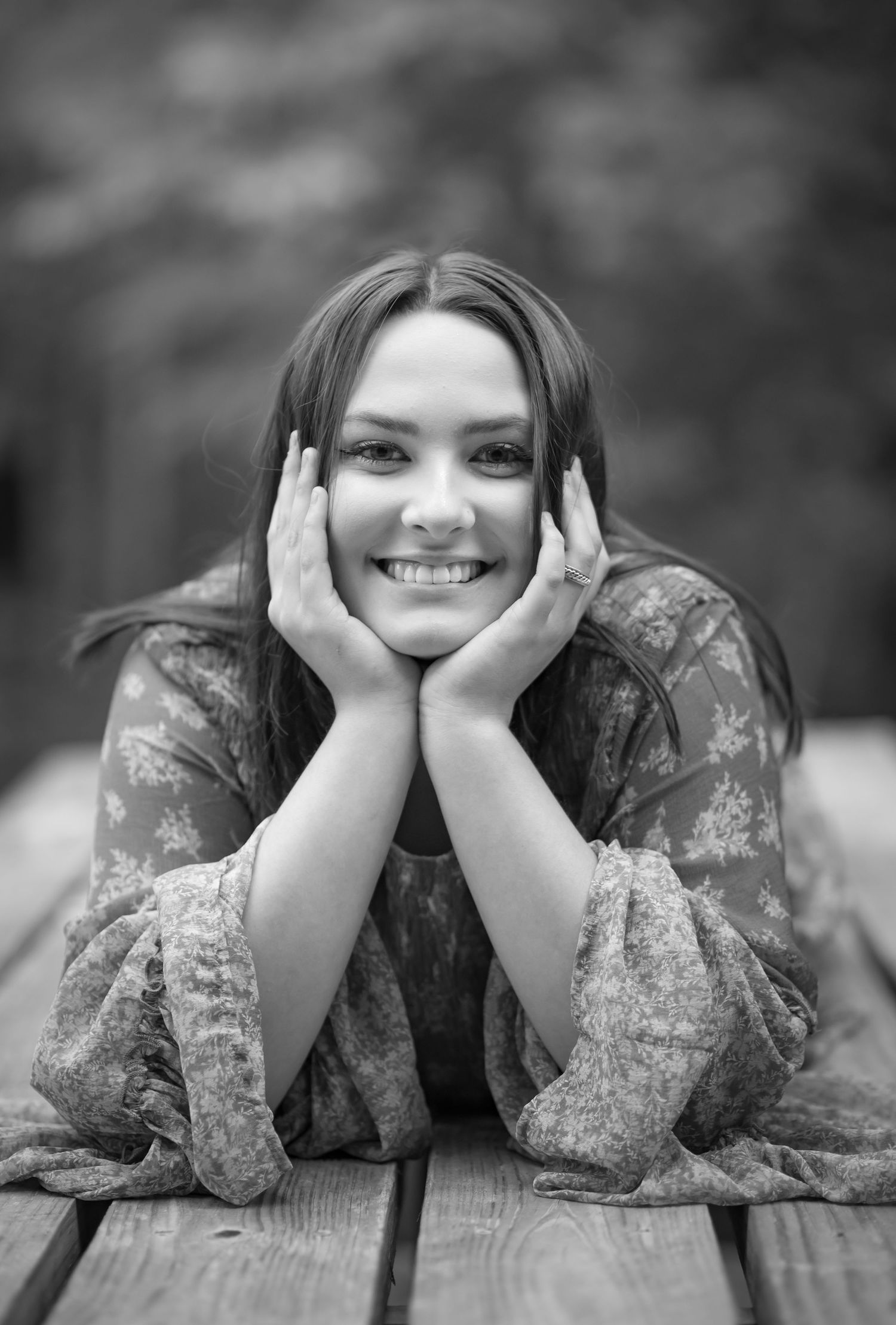 black and white portrait of a dark haired student, lying on her belly on a bench with her chin propped up in her hands and smiling