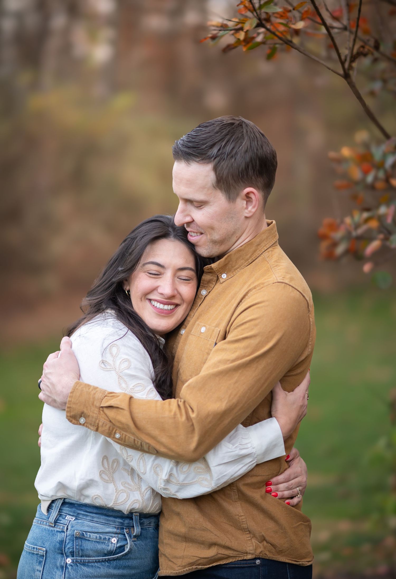 a dark haired woman in a white top laughs and snuggles against her husband as he hugs her