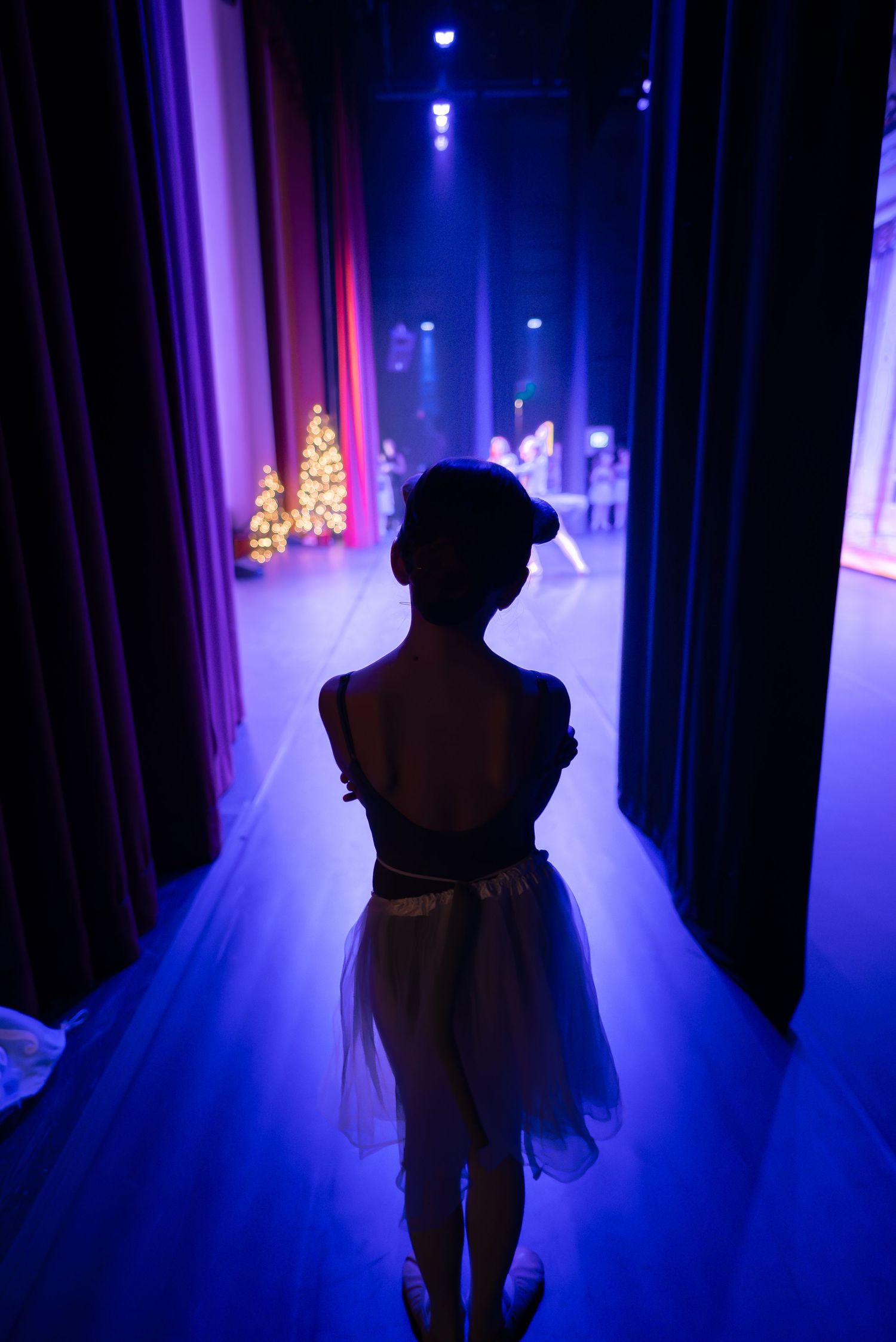 a young ballerina is silhouetted by the bright lights of the stage while waiting in the wings during a ballet performance