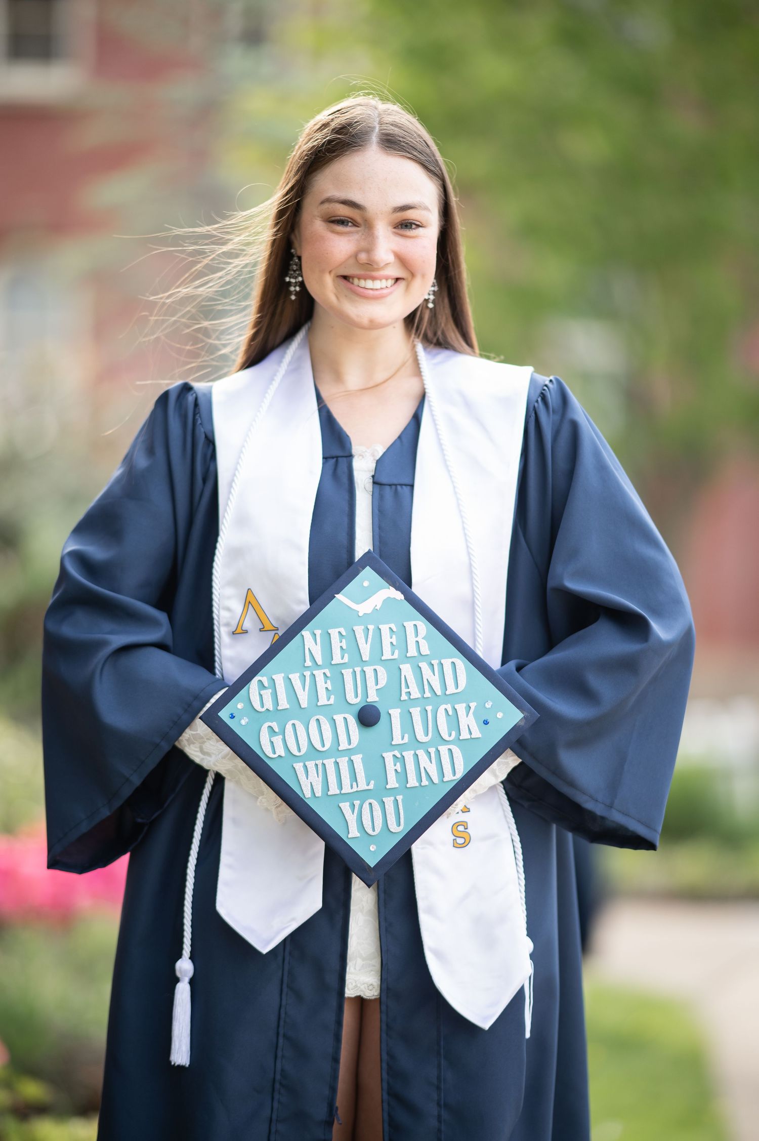 Smiling female graduate in navy cap and gown holding decorated mortarboard reading Never Give Up And Good Luck Will Find You.