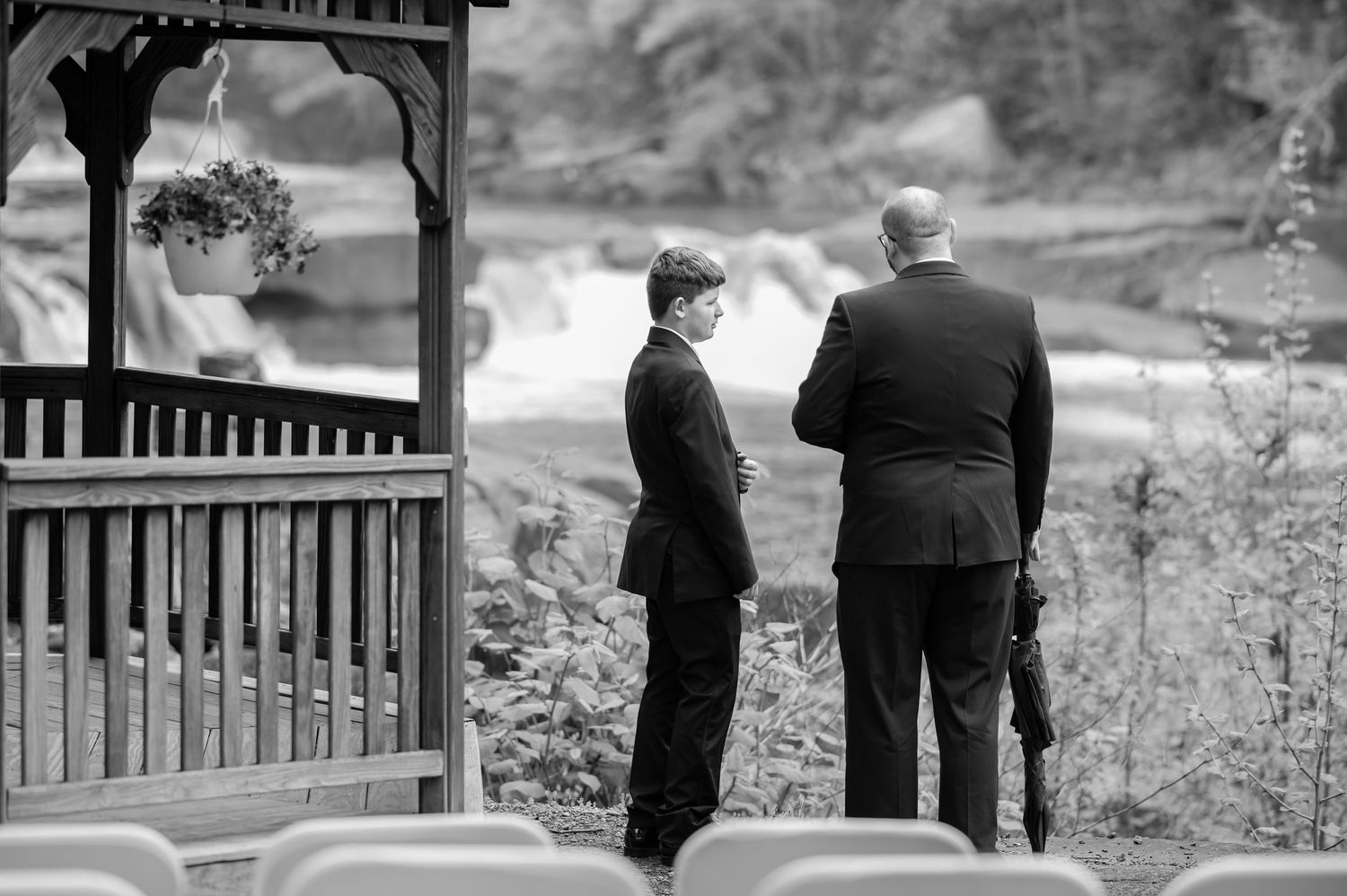 candid black and white image of a groomsman having a conversation with the bride's young son before the wedding ceremony