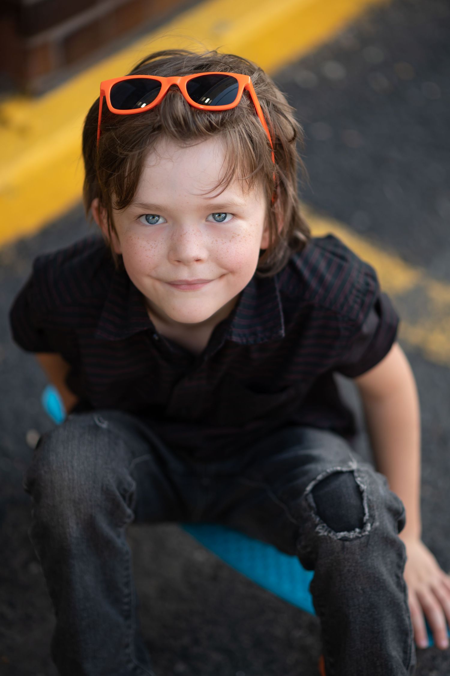closeup portrait of a little boy with tousled brown hair and freckles, looking up at the camera with a mischievous smile