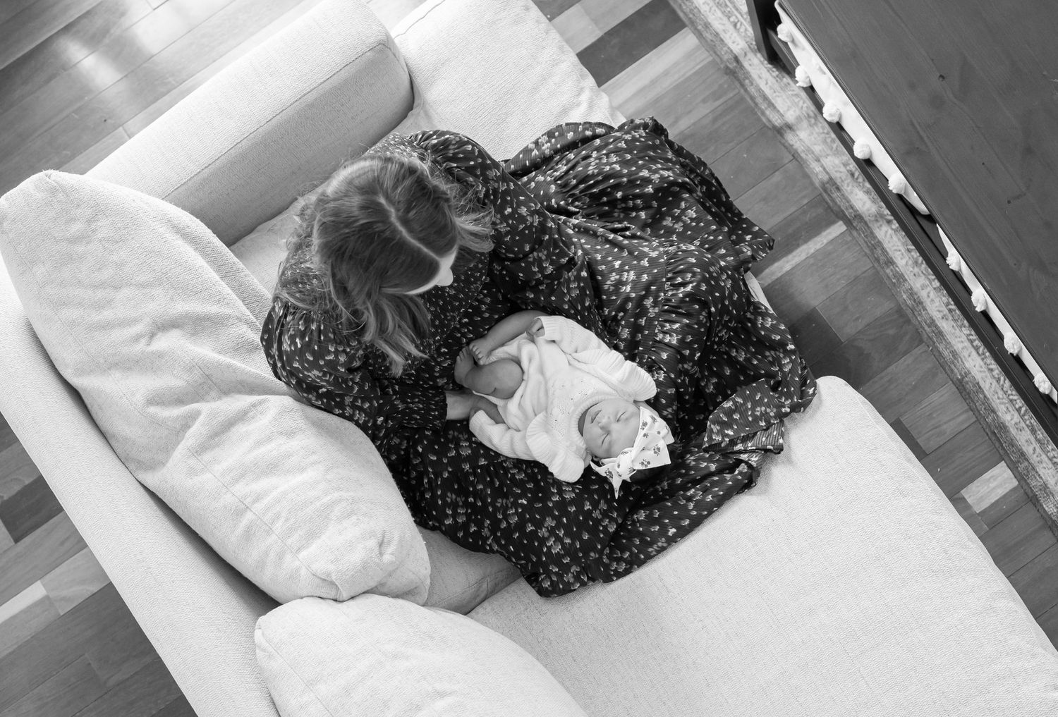 portrait shot from directly overhead, of. a mother in a dress seated on a white couch with her newborn baby on her lap