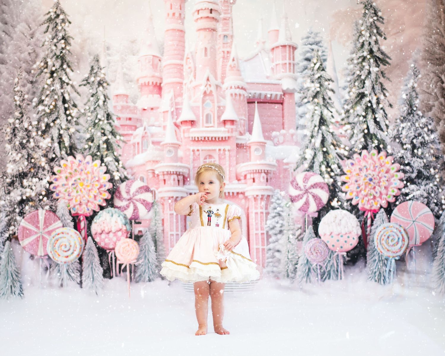 a little girl in a frilly pink christmas dress stands in the snow surrounded by giant lollipops, with a pink candy castle in the background