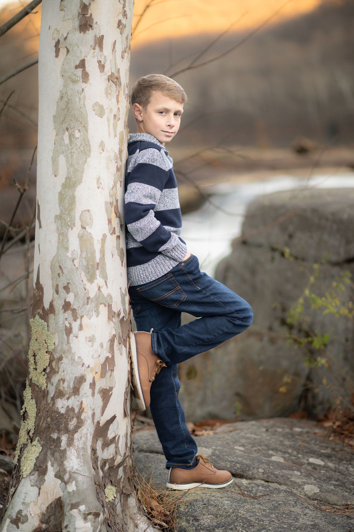 a handsome boy in a blue striped sweater and jeans leans against a tree with a river in the background, at Valley Falls State Park, WV