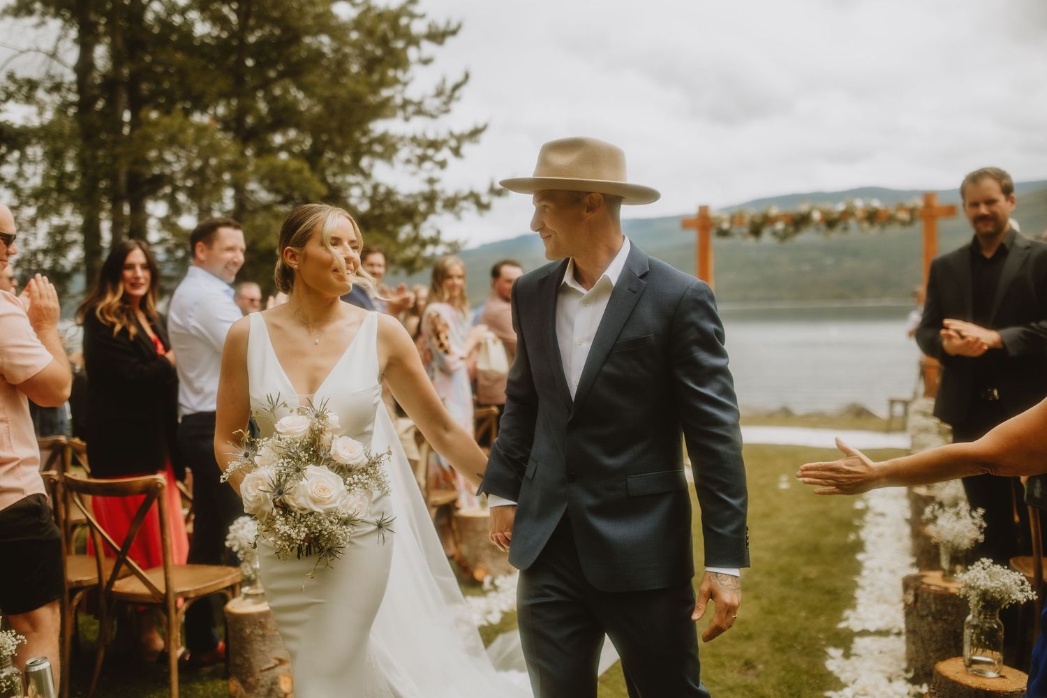 Newlywed couple walking down the aisle at outdoor lakeside wedding ceremony.