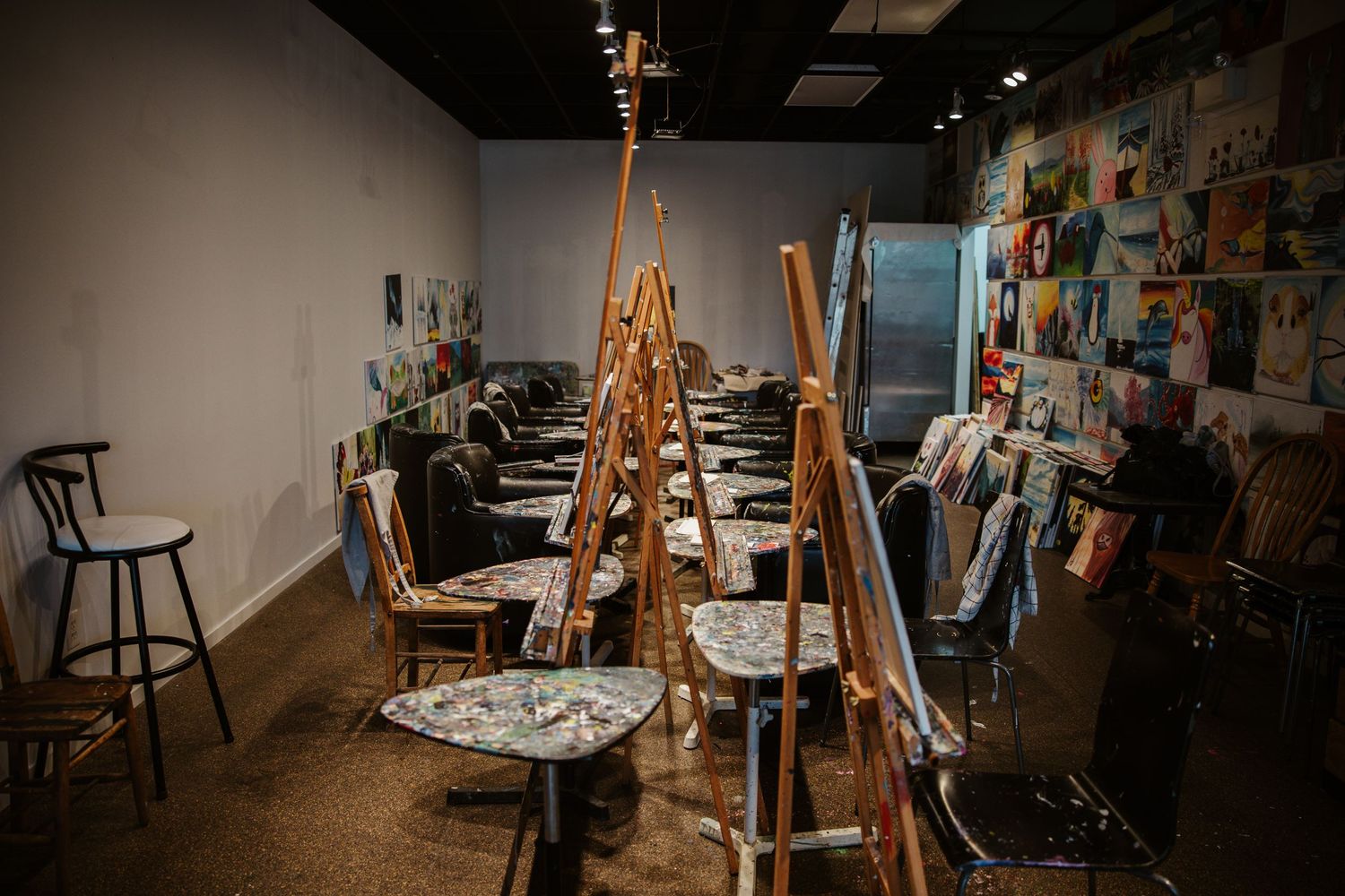 Empty art studio with wooden easels and stools arranged in rows.