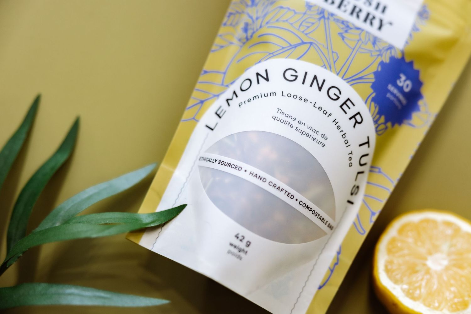 Bush Berry lemon ginger tea package with citrus and leaves on yellow surface.