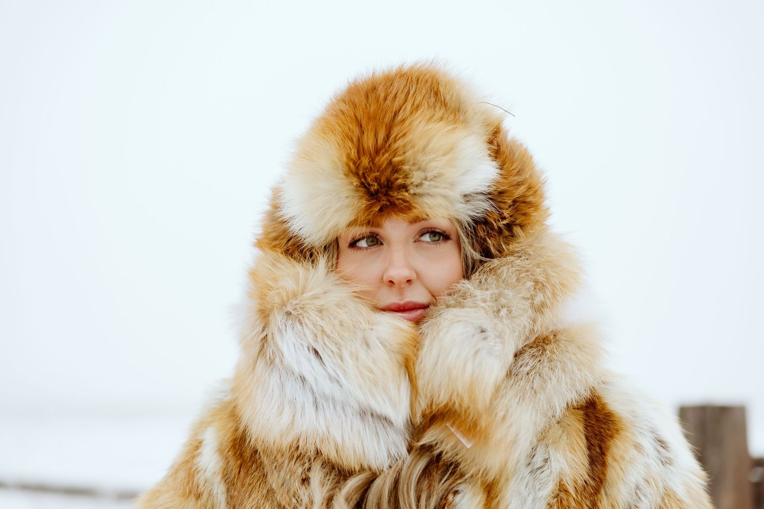 Winter fashion portrait featuring a plush fur hat and coat against snowy backdrop.