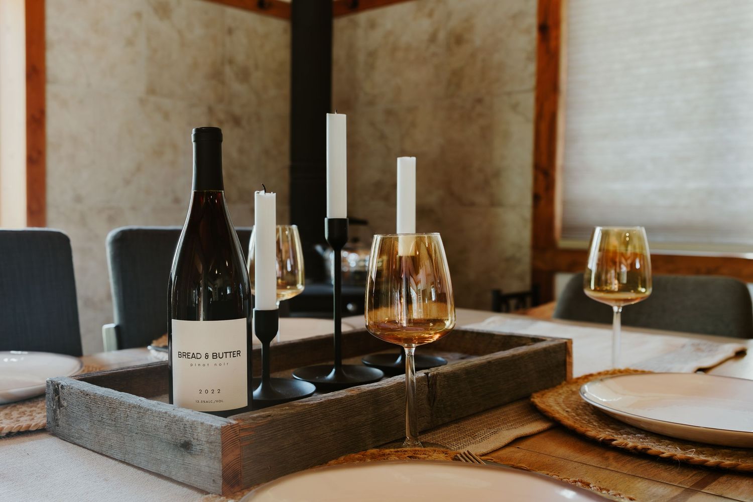 Wine tasting setup with bottles and glasses arranged on wooden tray with place settings.
