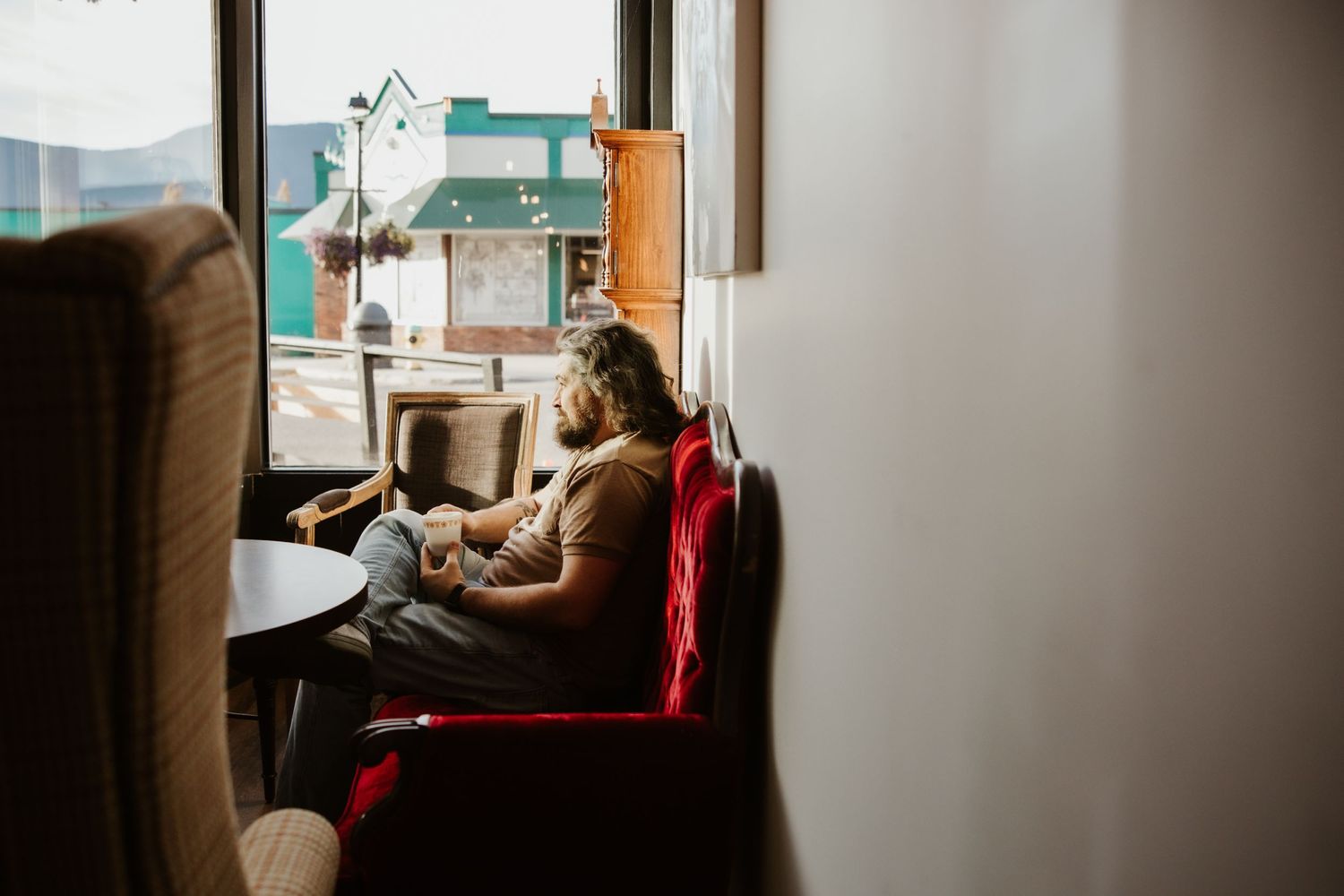 Person reading in cozy red armchair by window with natural light.
