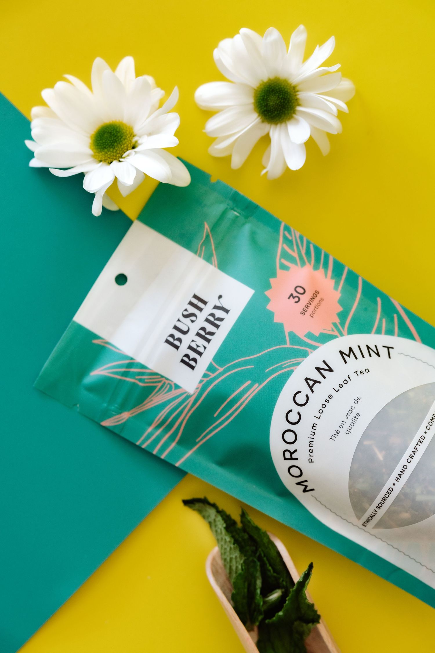 White daisies and moroccan mint tea packaging arranged on yellow and teal background.